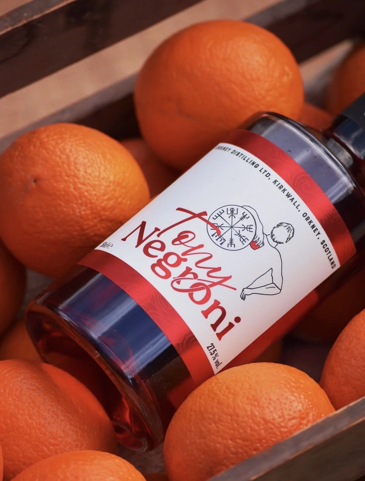 A bottle of Inverness whiskey lying among fresh oranges in a wooden container.