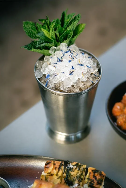 A metal cup filled with crushed ice and blue flower petals, garnished with fresh mint leaves.