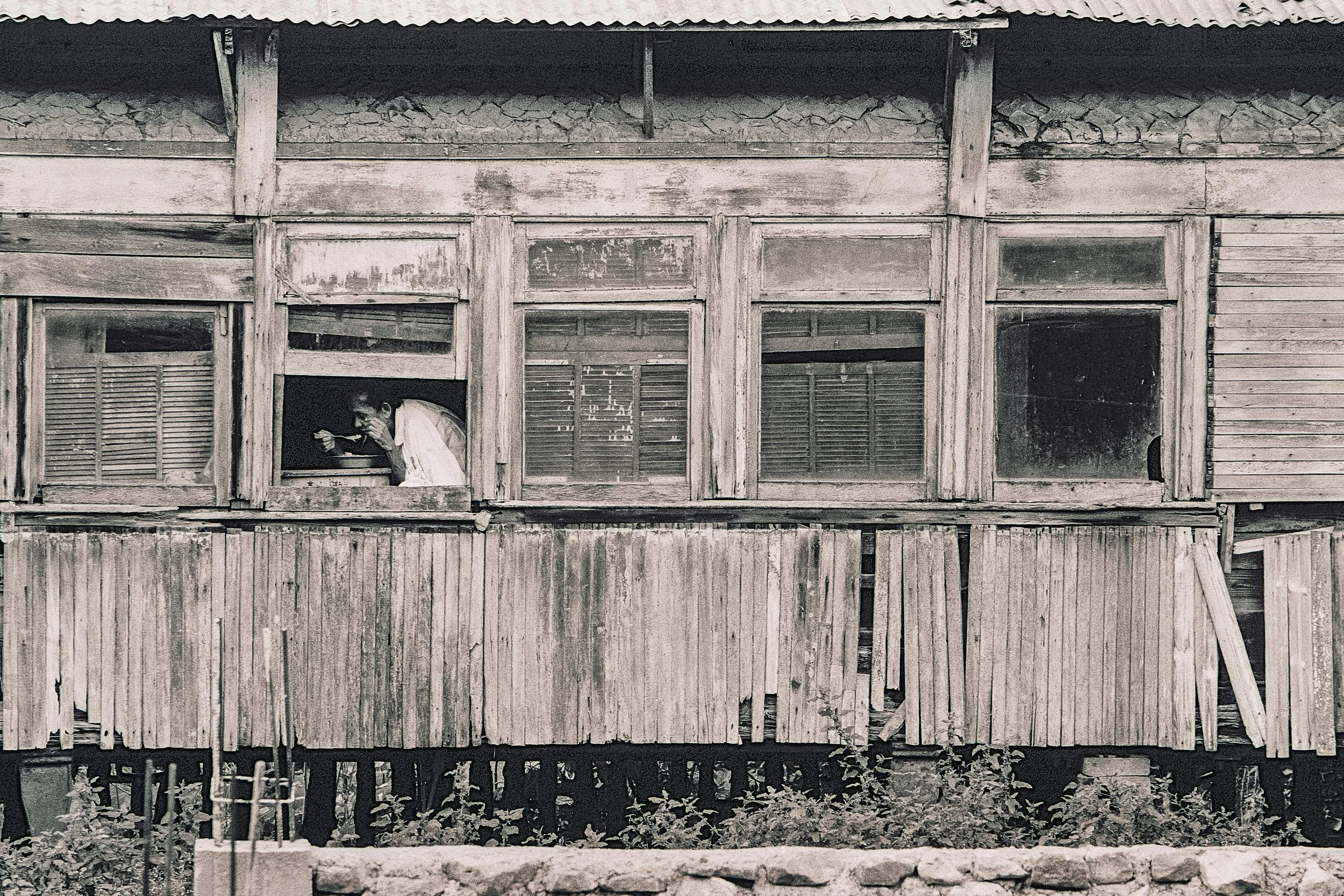 A person looking out of a window in an old, weathered wooden building.