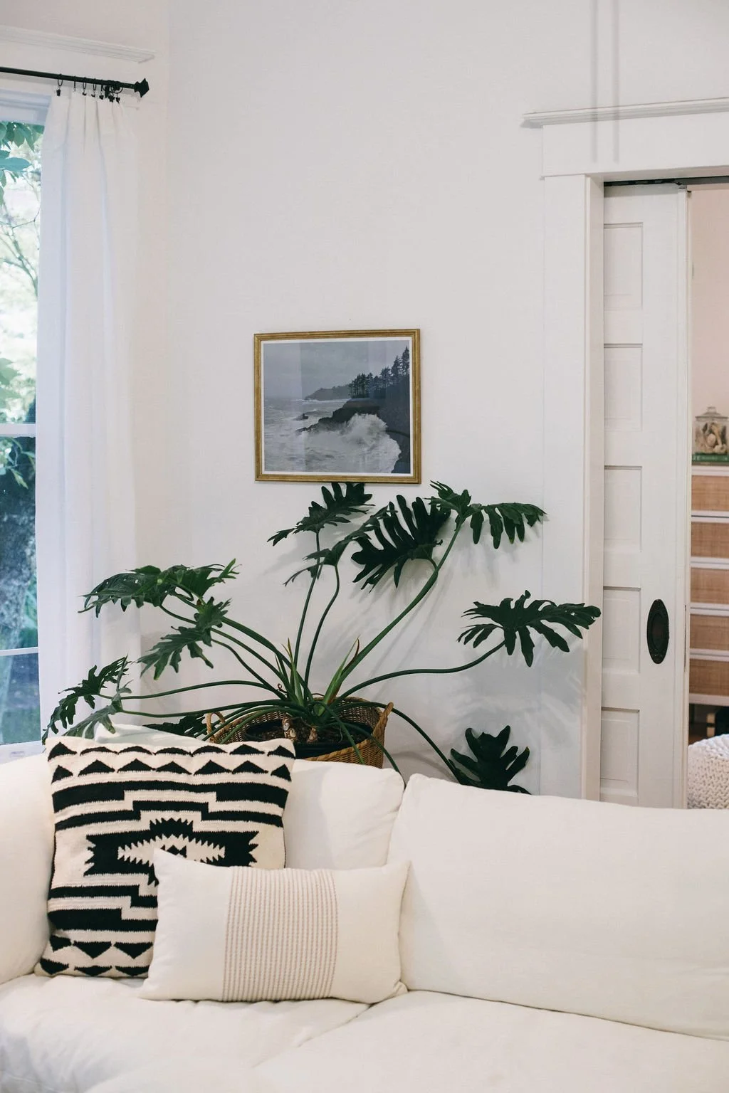 Inviting Portland  OR living room with a white sofa, black-and-white patterned pillow, large potted plant, coastal artwork, and soft natural light, showcasing the warm, layered interior design style of Linda McDermott and McDermott Interiors.