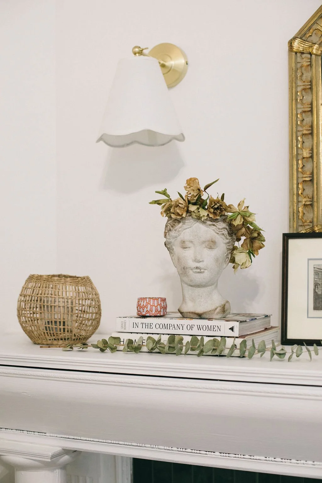 Decorative white mantel styled with books, flower vases, and a mirror, paired with a gold wall sconce and layered wall décor, showcasing the warm, timeless interior design aesthetic of McDermott Interiors in Portland, Oregon, serving the Portland