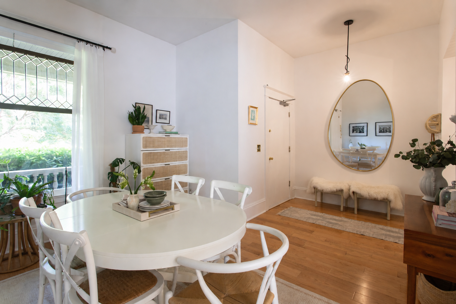 Dining room by Linda McDermott of McDermott Interiors, Portland, OR. A bright, modern dining space featuring a white oval table, sculptural chairs, lush greenery, a wood sideboard, and a large mirror that adds warmth, light, and timeless style.