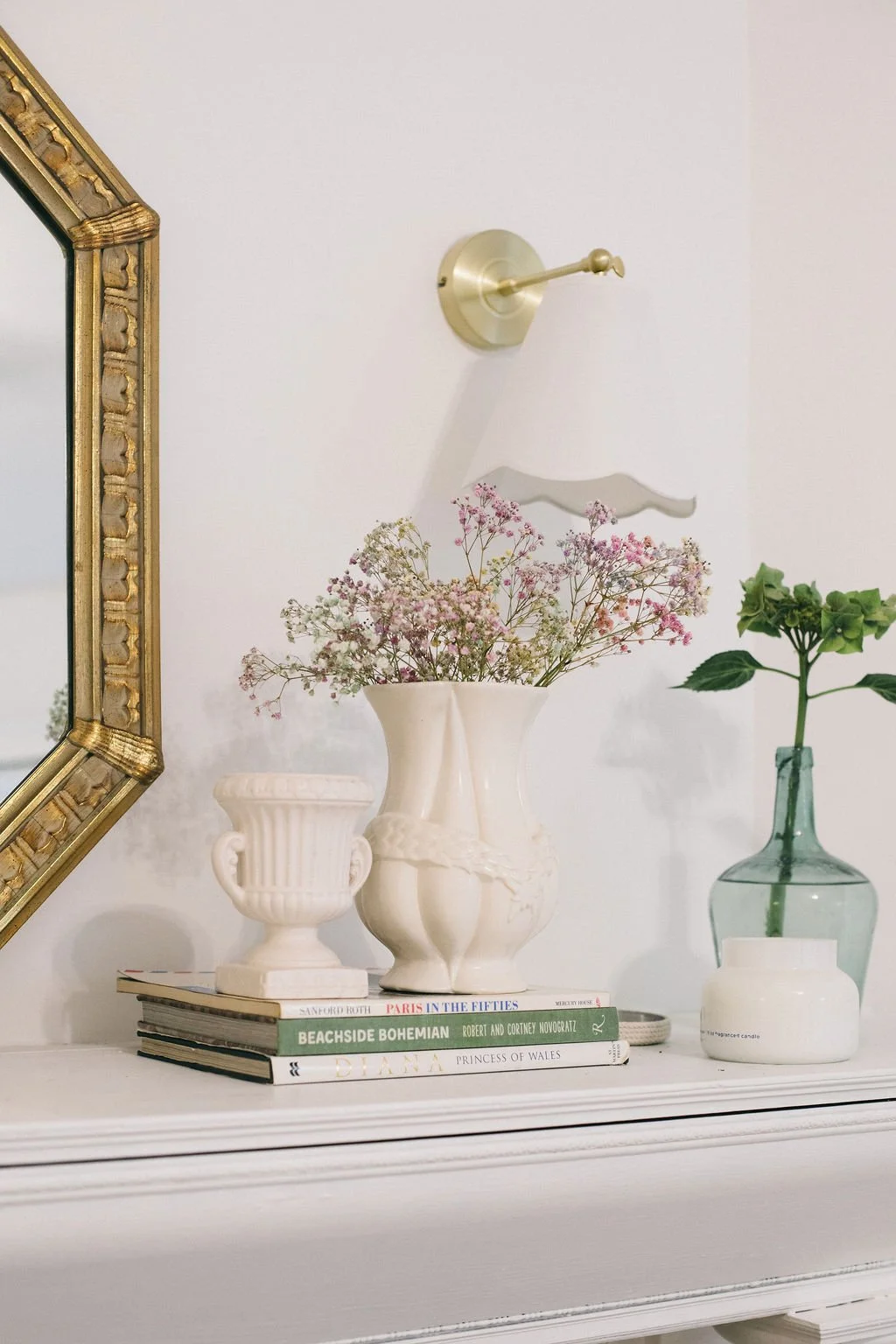 Decorative white mantel styled with books, flower vases, and a mirror, paired with a gold wall sconce and layered wall décor, showcasing the warm, timeless interior design aesthetic of McDermott Interiors in Portland, Oregon, serving Portland Metro.