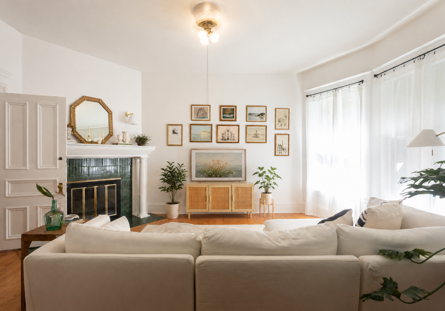 Portland, OR living room designed by Linda McDermott of McDermott Interiors, featuring a striking green tiled fireplace, white sofa, curated framed artwork, warm wood accents, lush greenery, and abundant natural light. This Portland interior design c