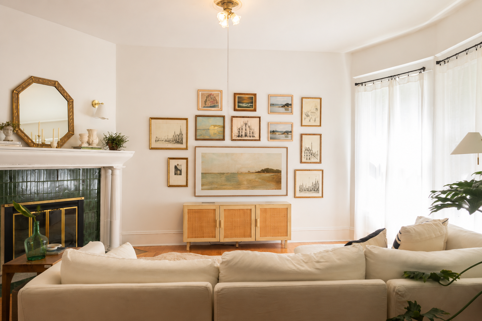 Living room by Linda McDermott of McDermott Interiors, Portland, OR. A bright, welcoming space featuring a cream sectional, green tile fireplace, curated gallery wall, and large windows softened with sheer curtains.