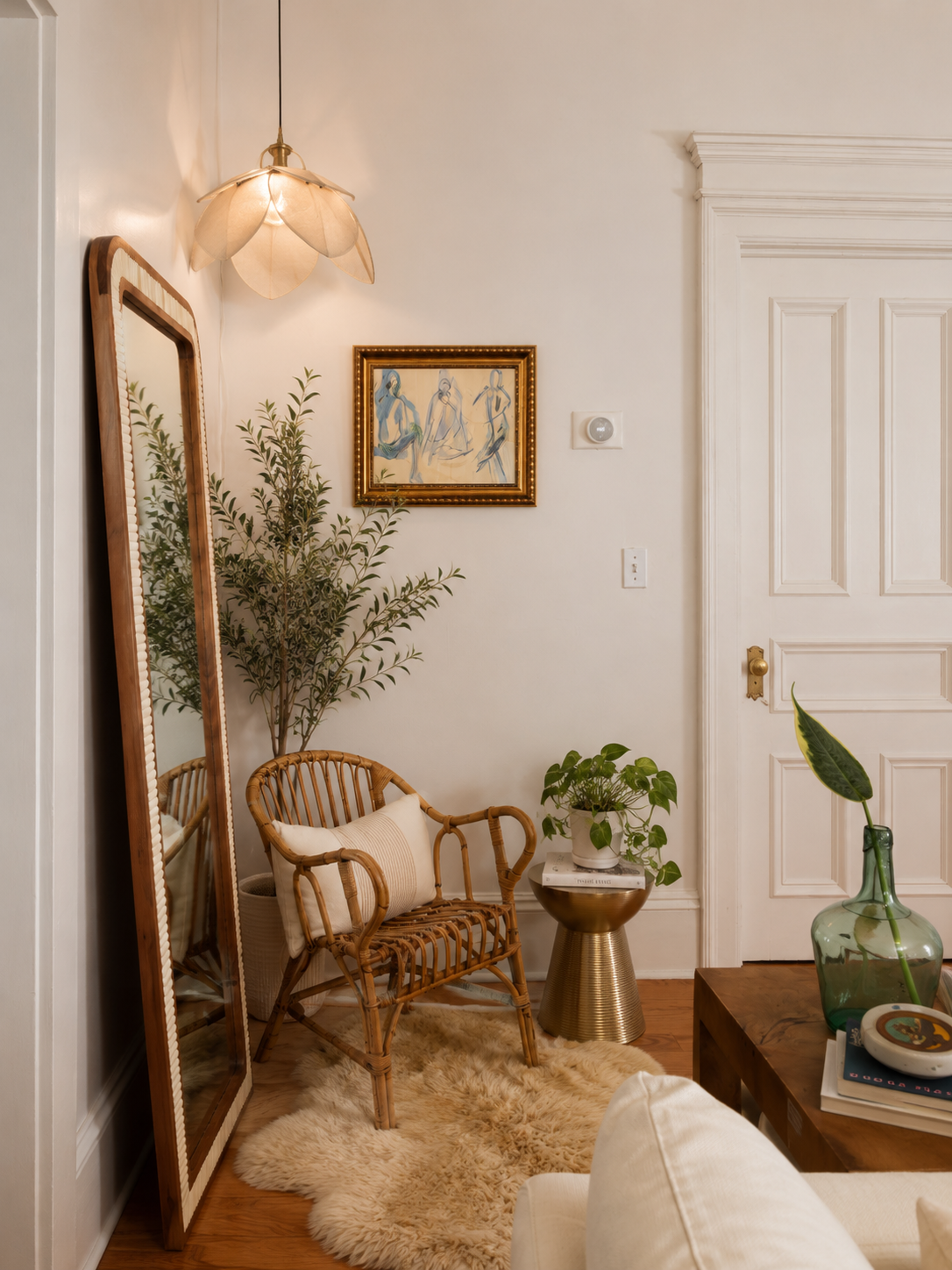 Living room by Linda McDermott of McDermott Interiors, Portland, OR. A cozy corner featuring a leaning mirror, woven chair, lush greenery, abstract artwork, and layered textures for a warm, inviting feel.