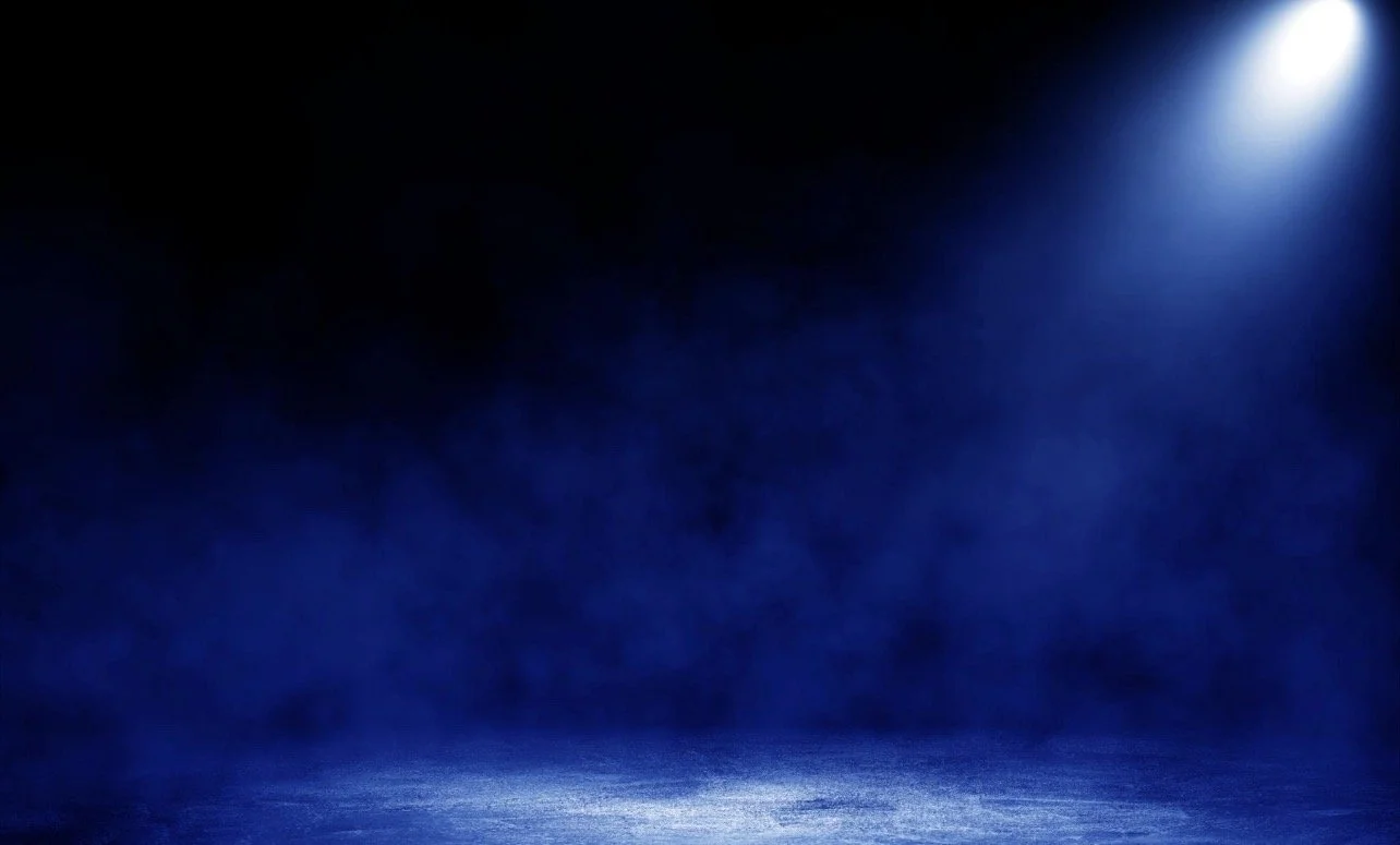 Dark stage with blue lighting and a spotlight shining down on the floor.
