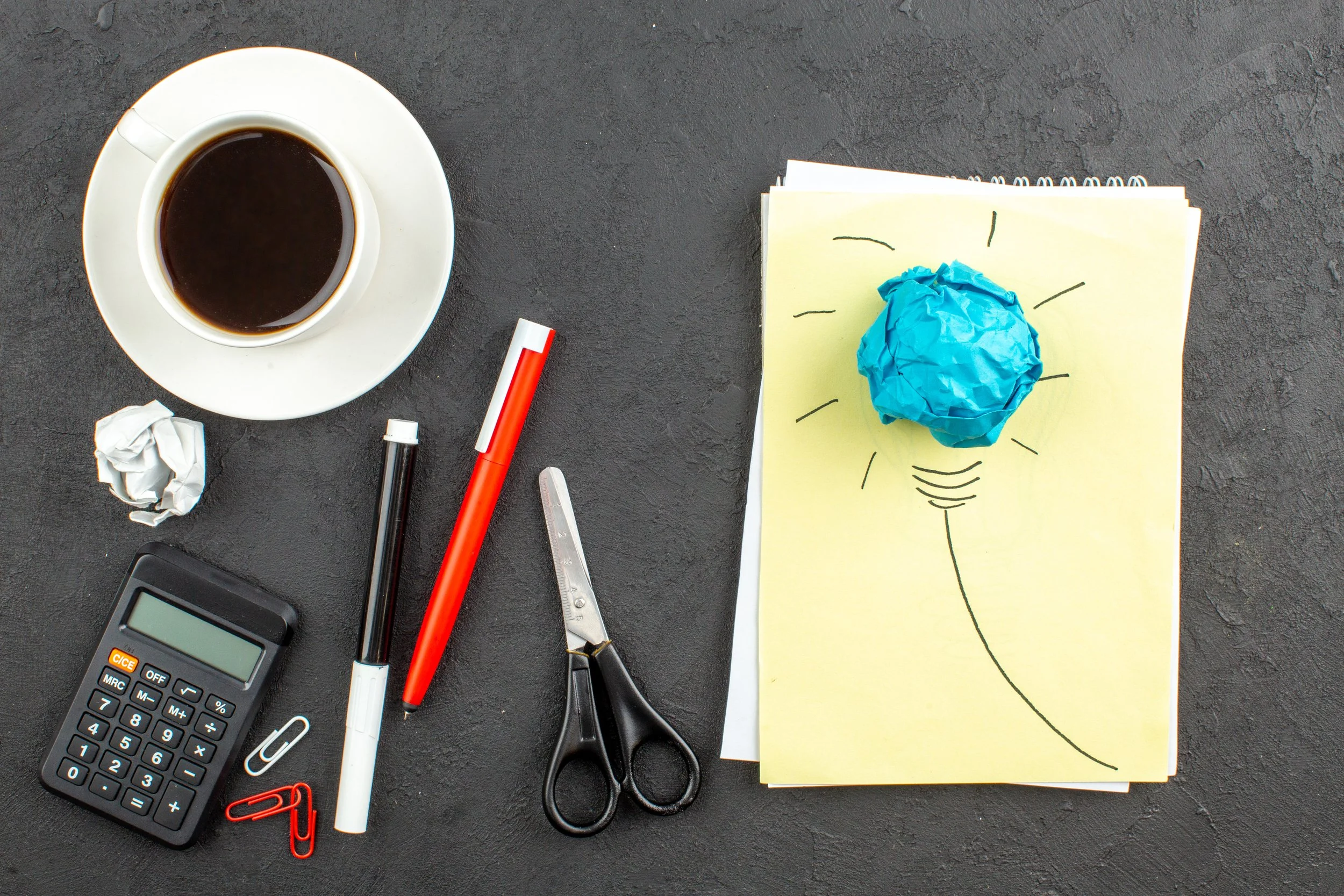 top-view-idealight-bulb-notepad-scissors-calculator-cup-tea-red-pen-black-marker-black.jpg