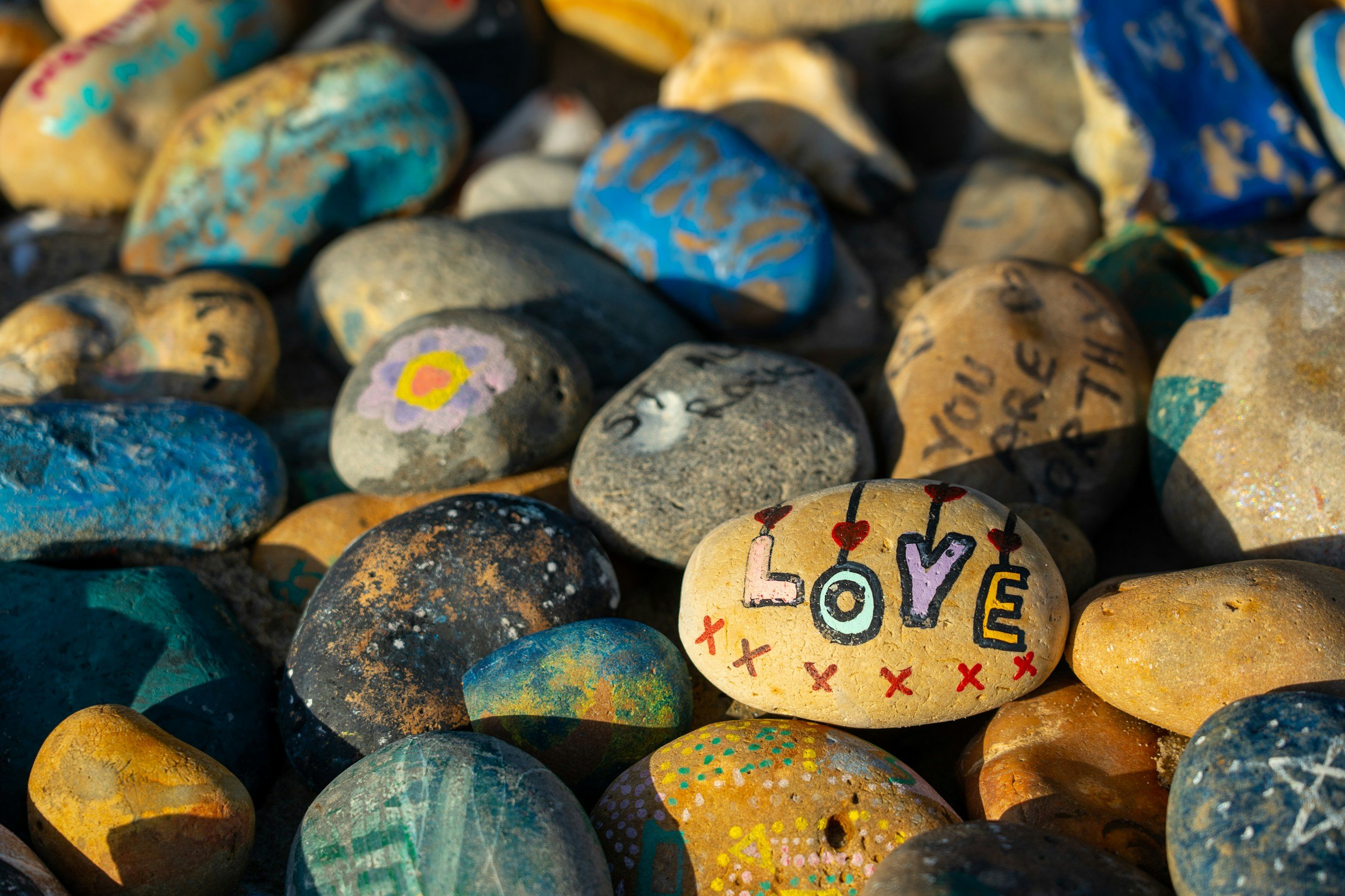 Colorful painted rocks with one prominently displaying the word 'LOVE' with hearts and Xs.