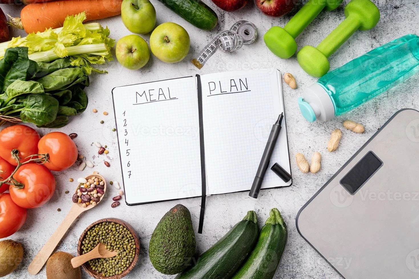 A meal planning setup on a table with fresh vegetables and fruits surrounding a notebook labeled 'Meal Plan' with a pen. Items include tomatoes, lettuce, celery, green apples, cucumbers, zucchini, carrots, an avocado, various beans and pulses, a measuring tape, a water bottle, a scale, and a few peanuts.
