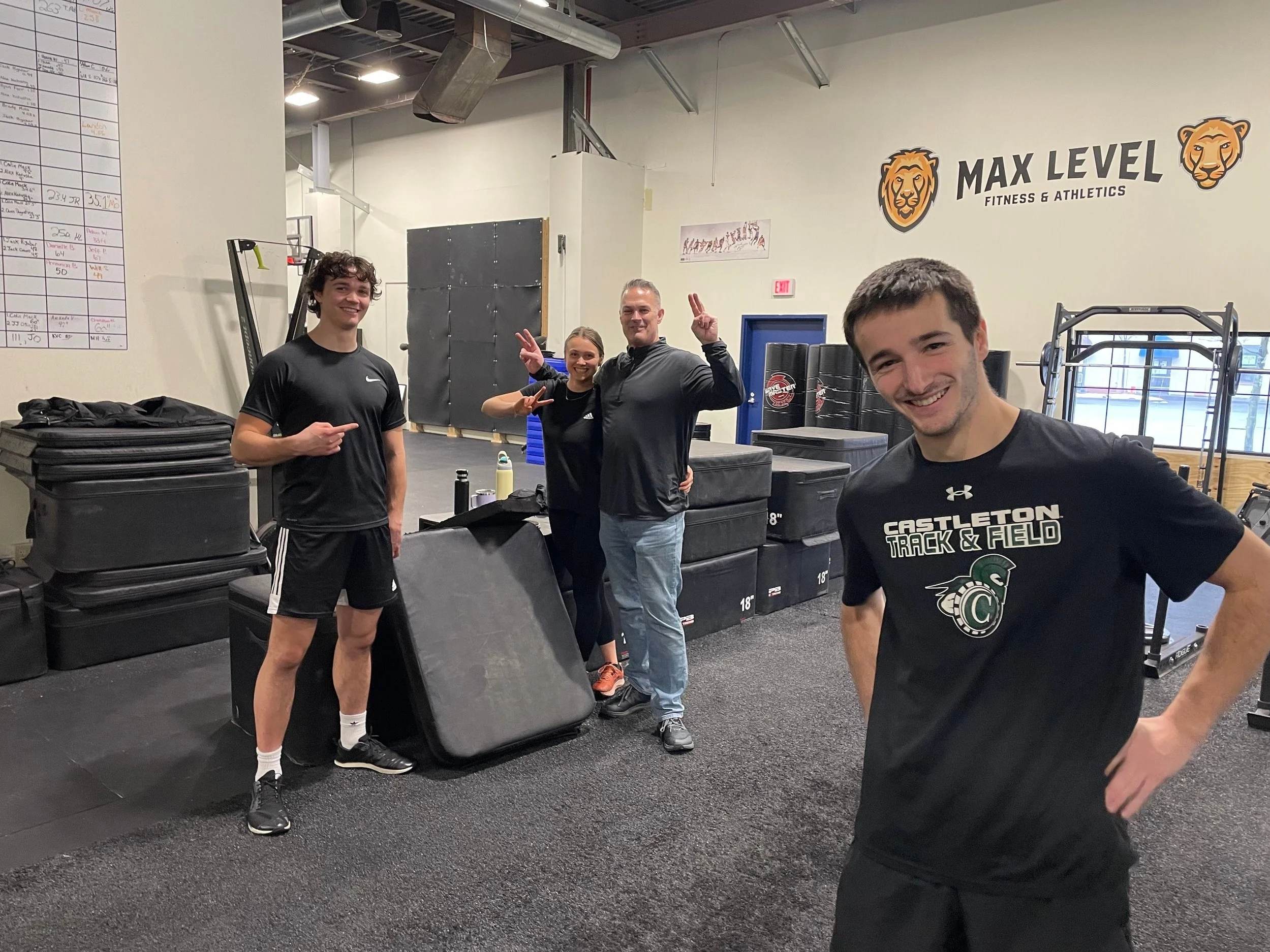 Goodemote Sports & Performance staff posing inside a gym, with weight training equipment and a sign reading 'MAX LEVEL FITNESS & ATHLETICS' in the background.