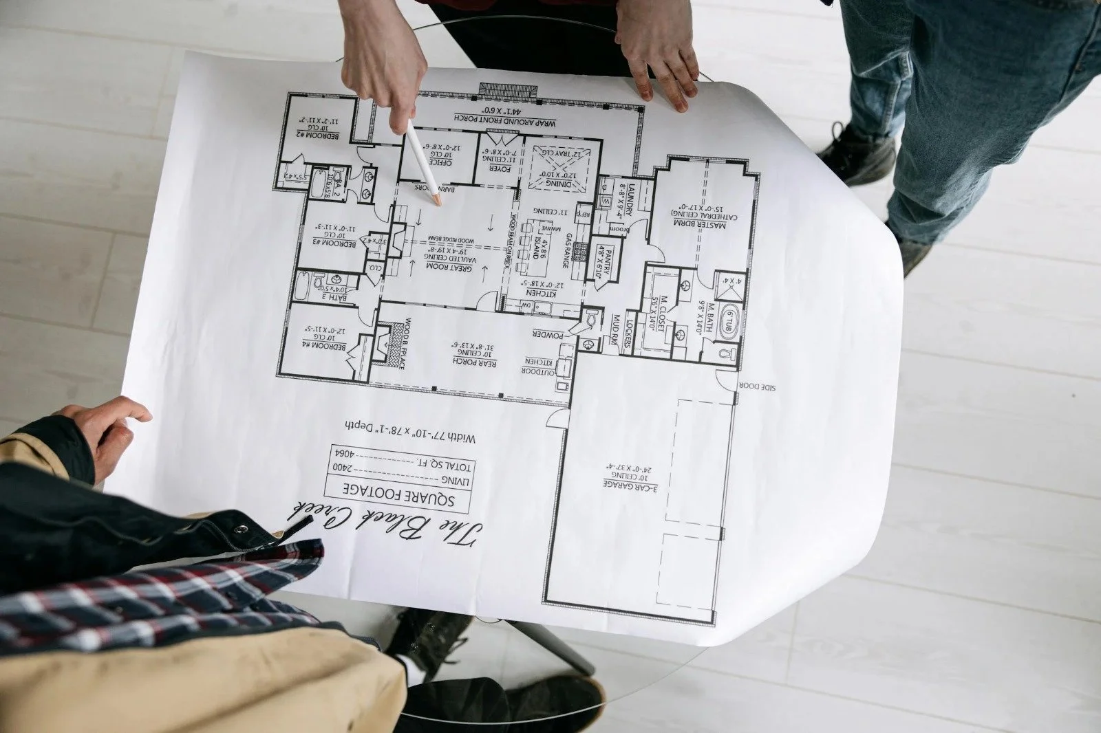 Two people examining a house blueprint or floor plan laid out on a table.