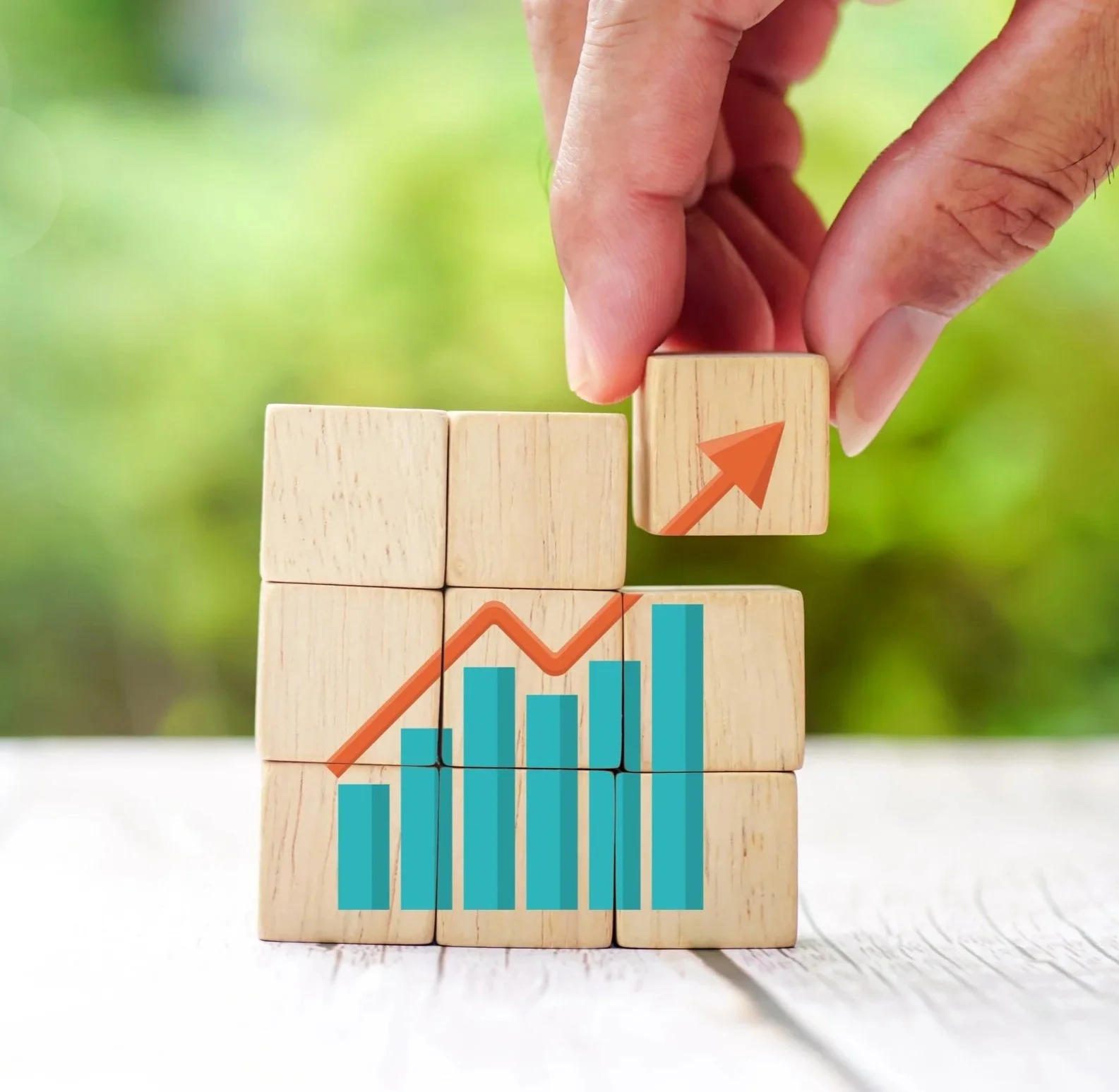 Hand stacking wooden blocks with graph and upward arrow, symbolizing growth and progress.
