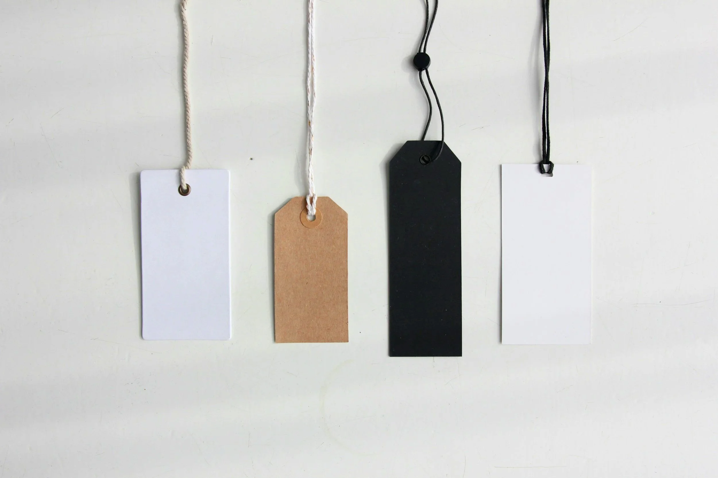 Four blank tags hanging on a white background, each with a different color and string.