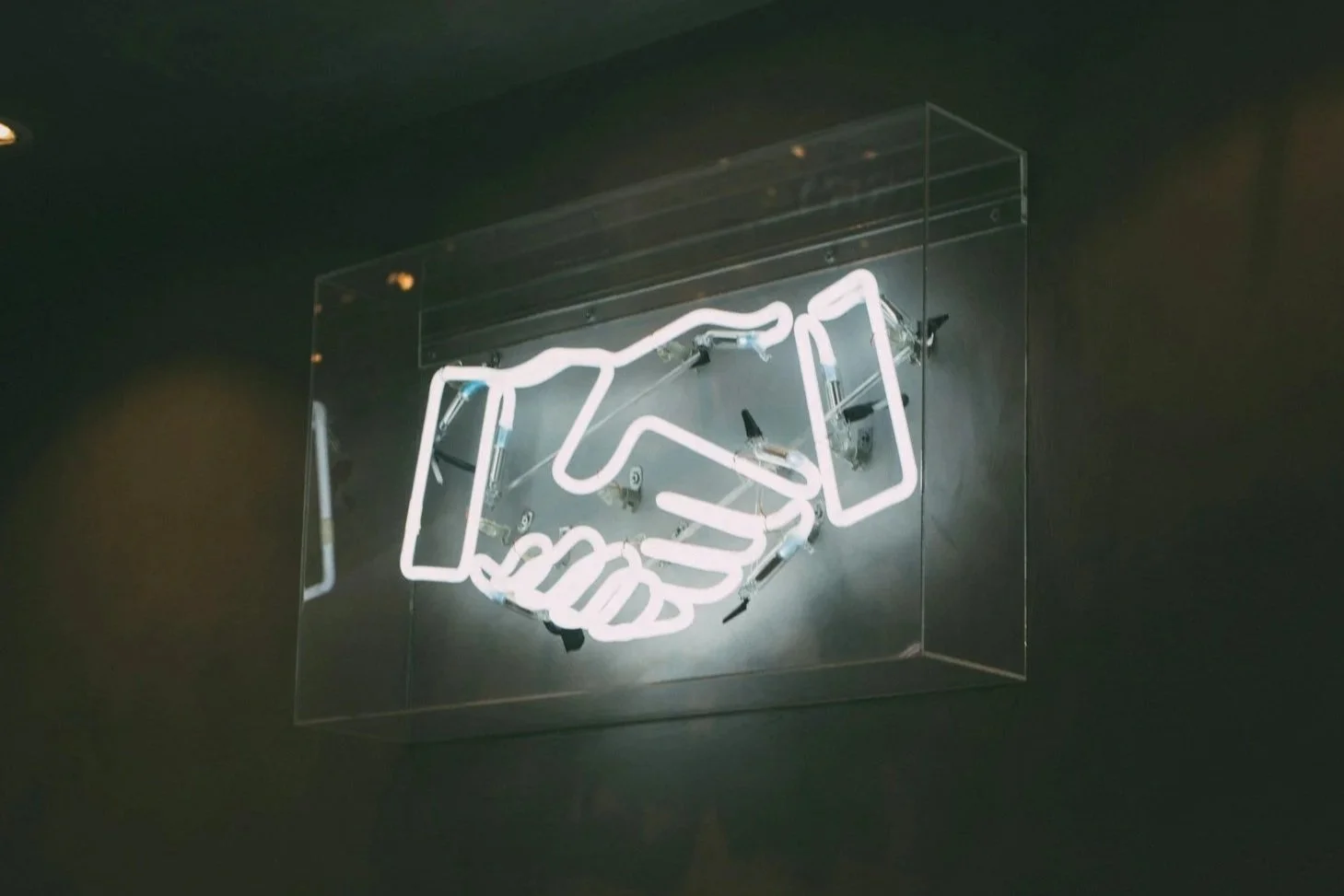 Neon sign depicting a handshake mounted on a wall.