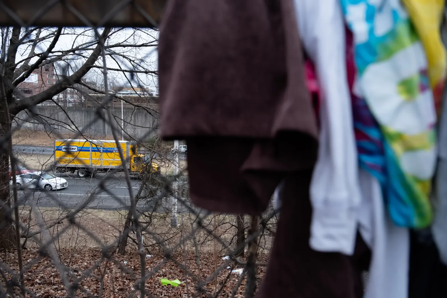 Clothes hanging on a fence with trees and cars on a street in the background.