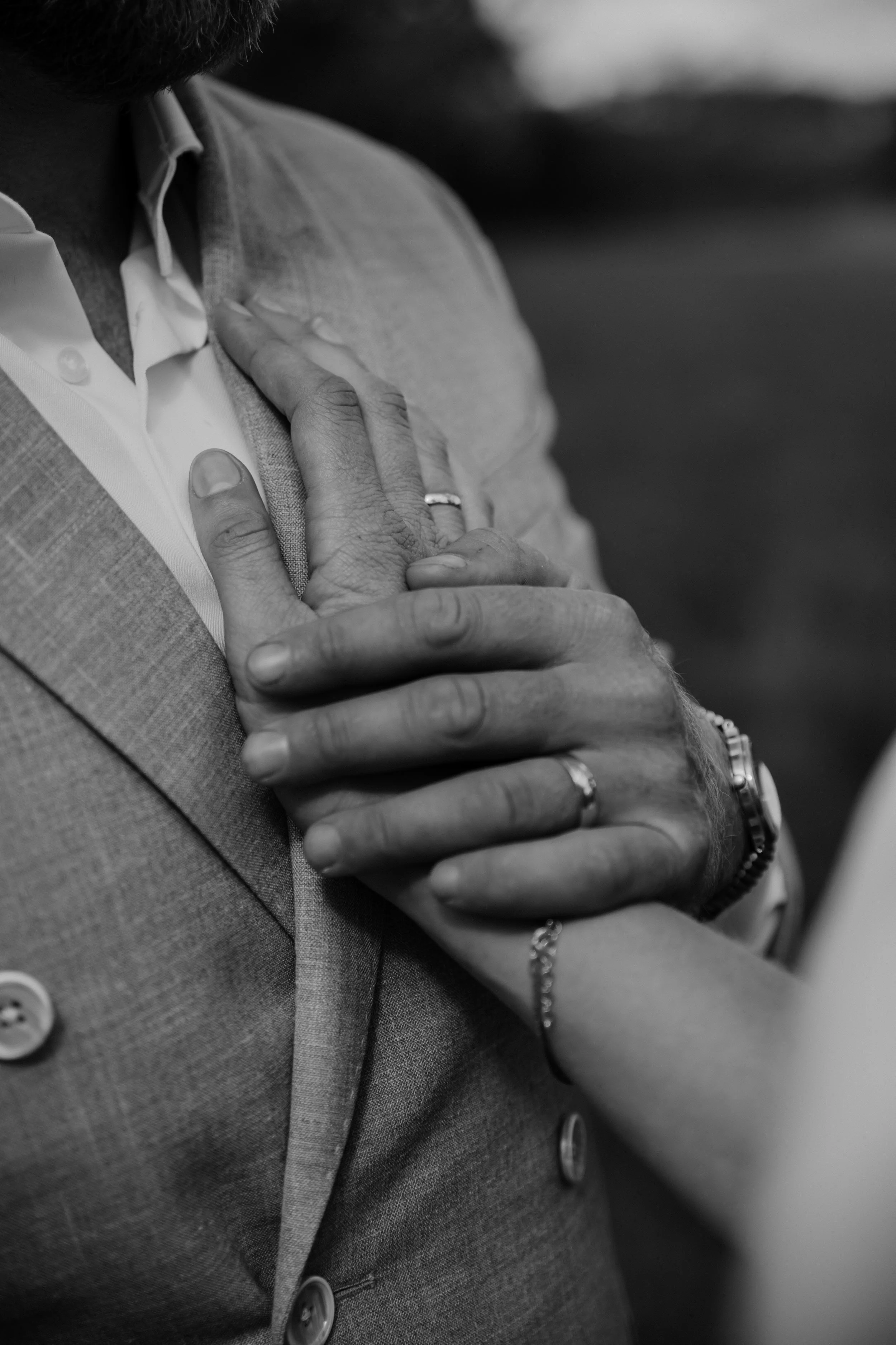 Close-up van een man die een hand op zijn borst legt, gekleed in een grijs pak en een witte overhemd, in zwart-wijn
