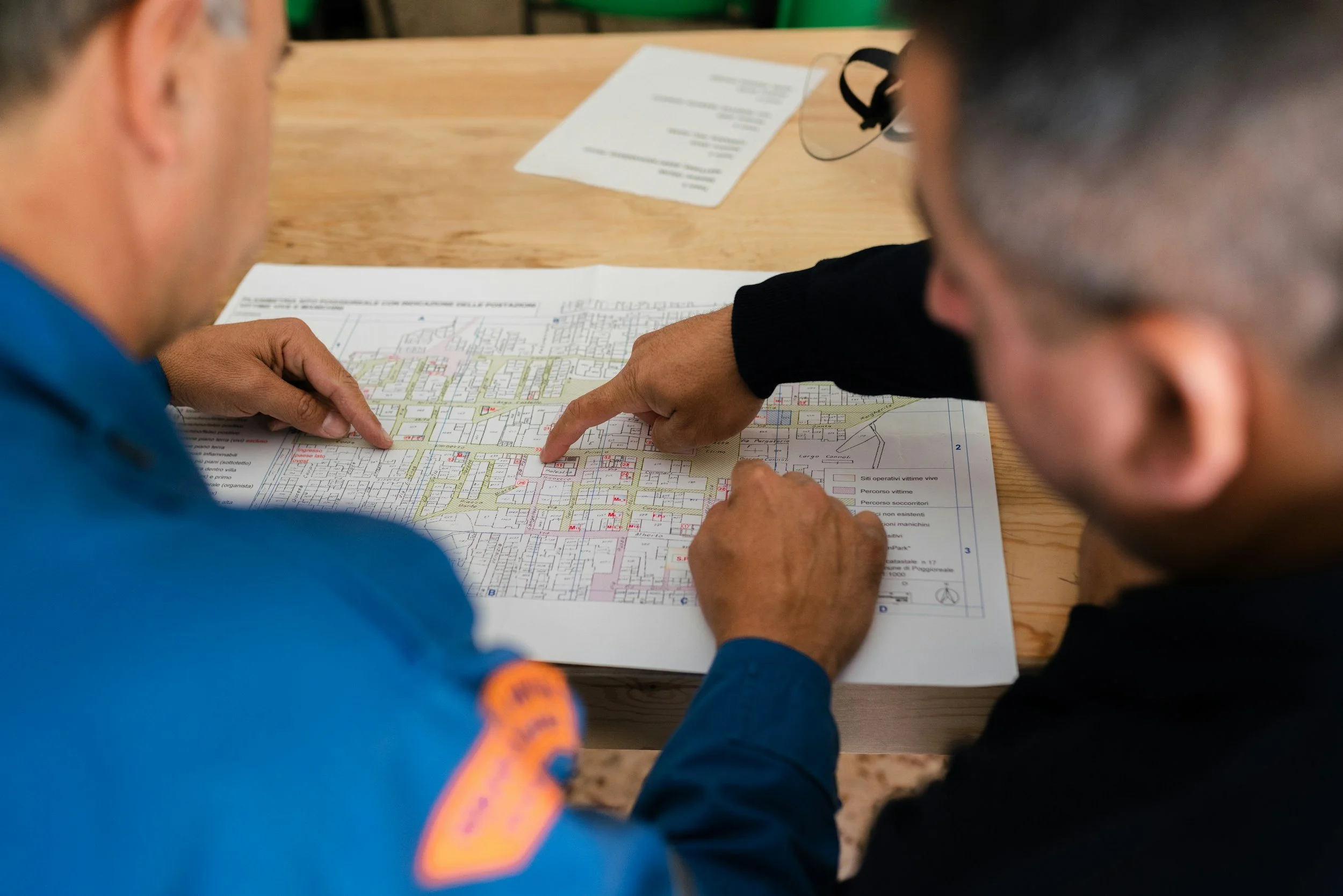Two men look at a city map on a table, with one pointing at a specific location.