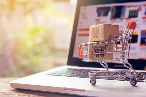 Miniature shopping cart with a small cardboard box inside sitting on a laptop keyboard.