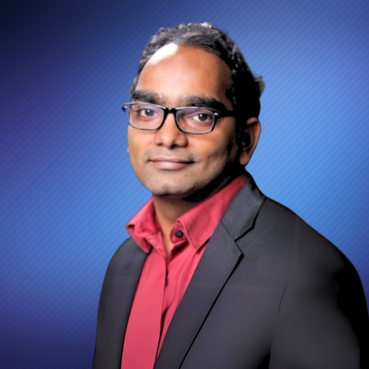 Professional headshot of a man with glasses, wearing a black blazer and red shirt, against a blue gradient background.