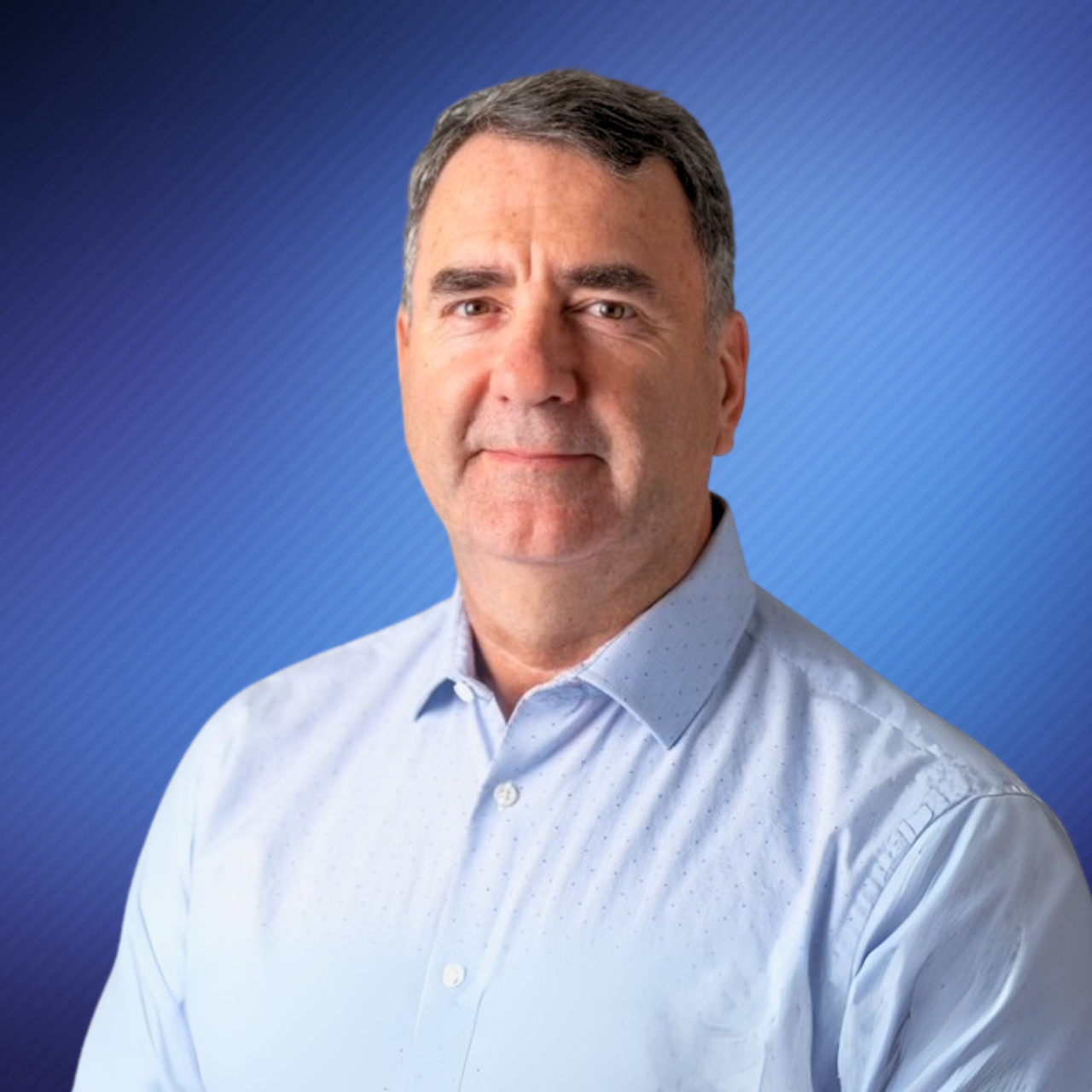 Portrait of a middle-aged man with short dark hair, wearing a light blue button-up shirt, standing against a blue gradient background.