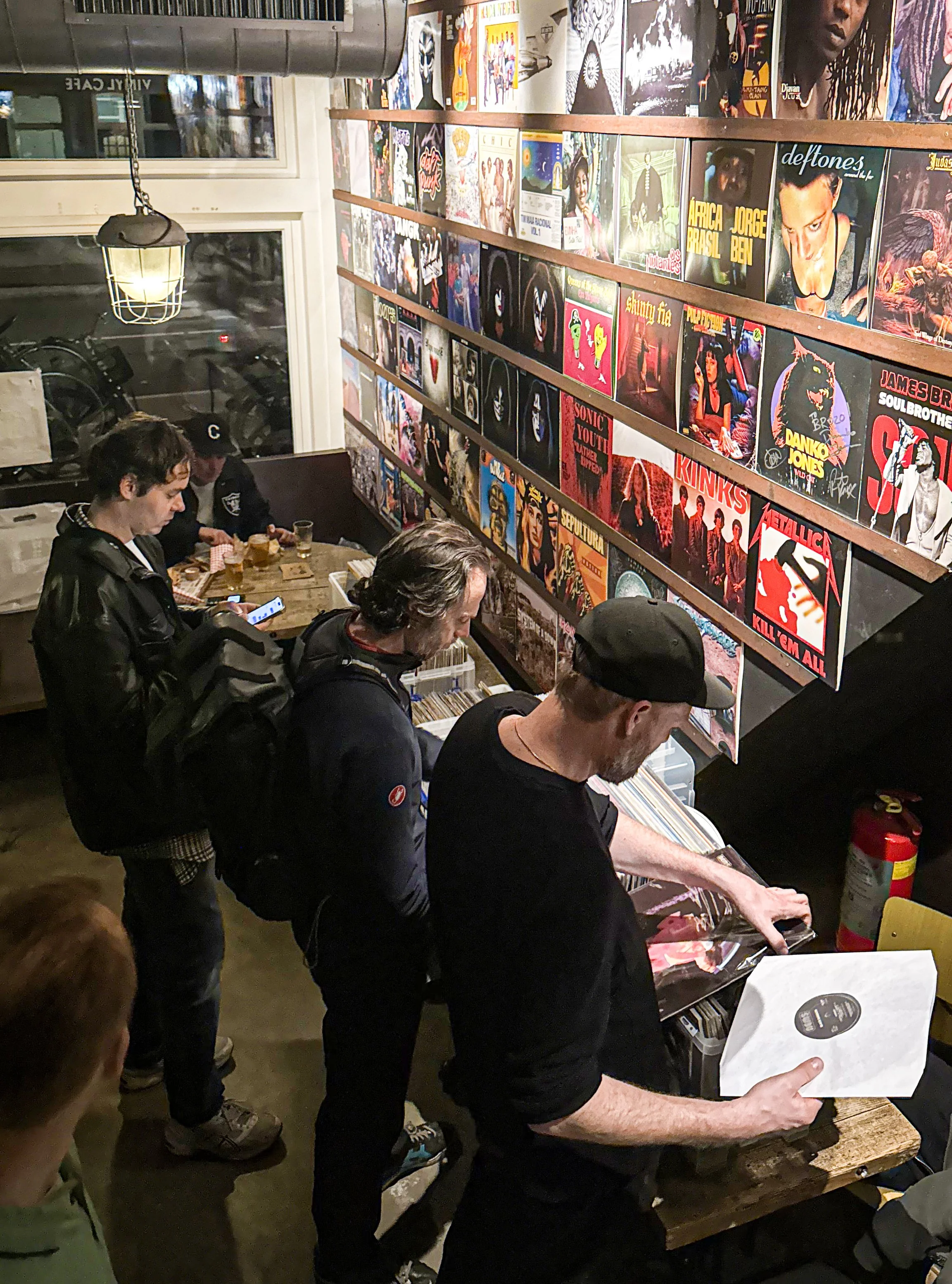 Group of people browsing vinyl records in a record store with a wall full of album covers.