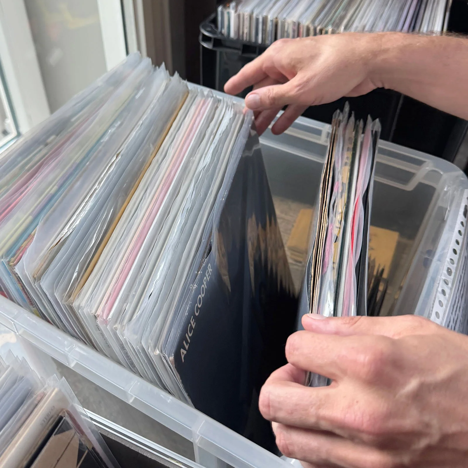 Close-up of a person's hands flipping through plastic sleeves containing vinyl records at an Amsterdam Vinyl Club live event.