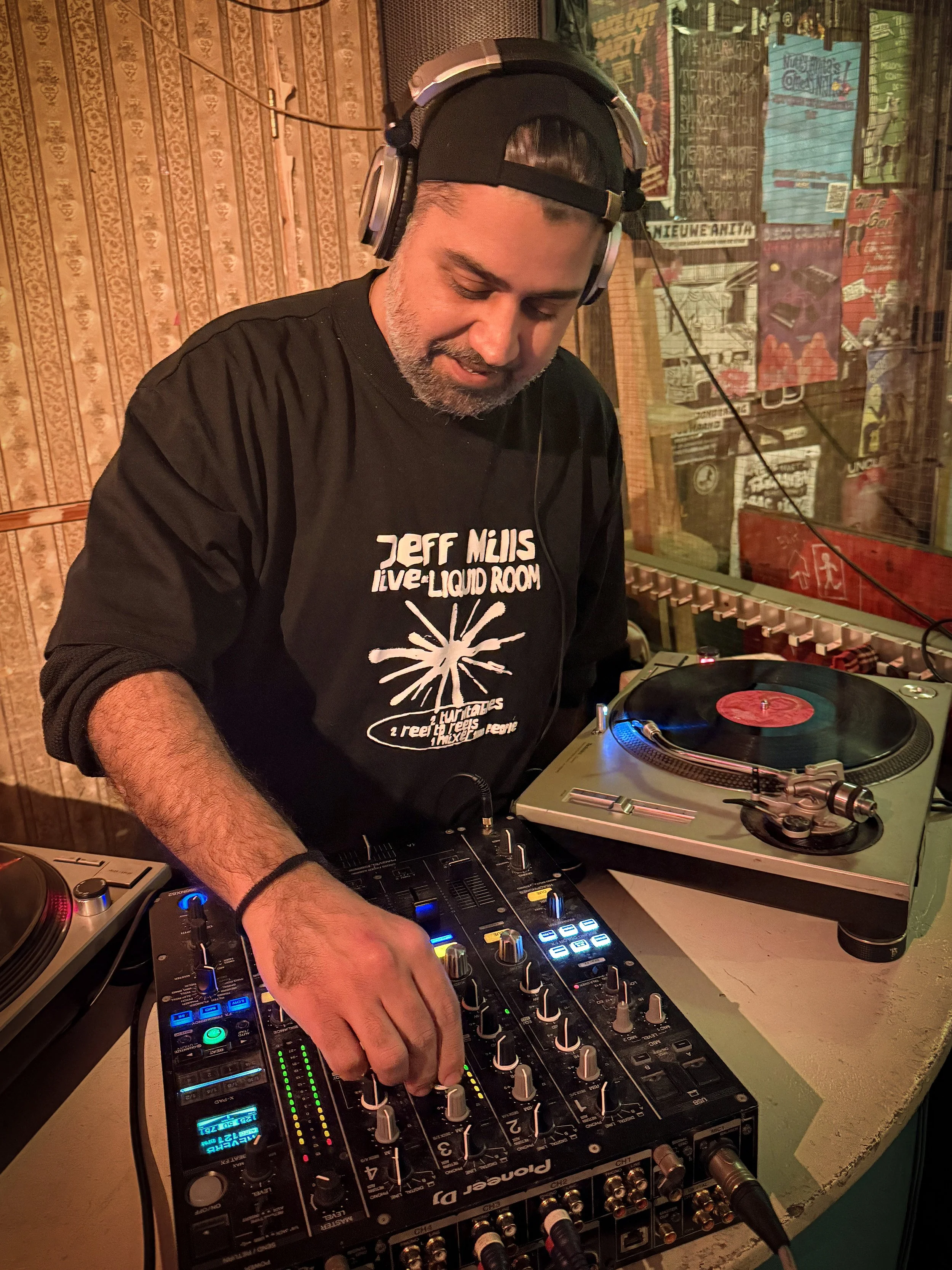 Deepkak Nichani playing a guest DJ set at Amsterdam Vinyl Club. He's wearing headphones and a black T-shirt.