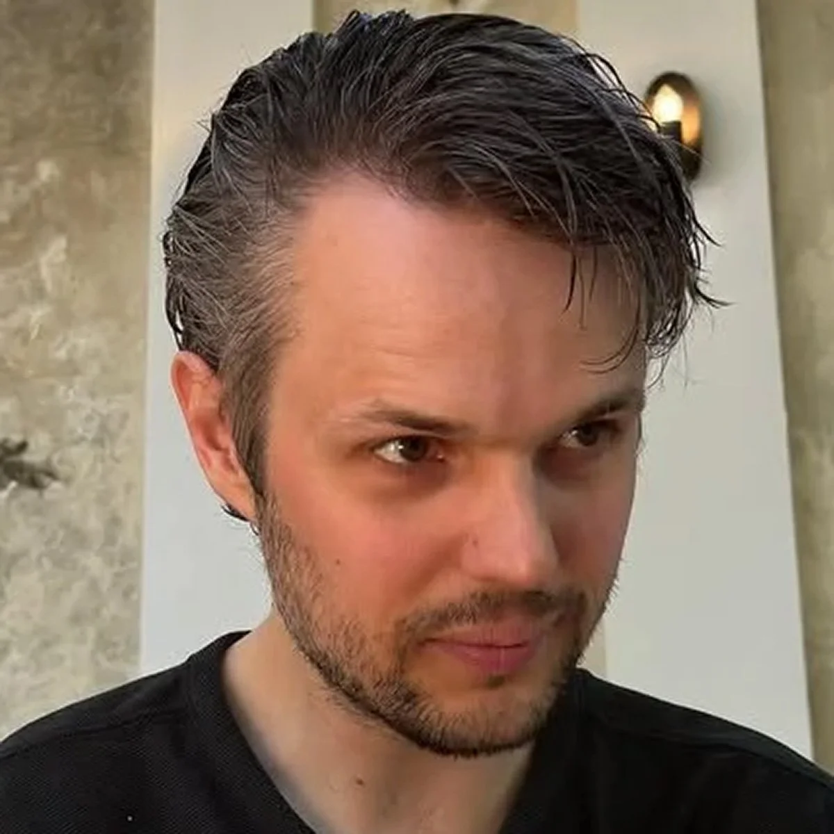 A portrait of DJ Boudweijn - man with dark, slicked-back hair and a short beard looking slightly downward.