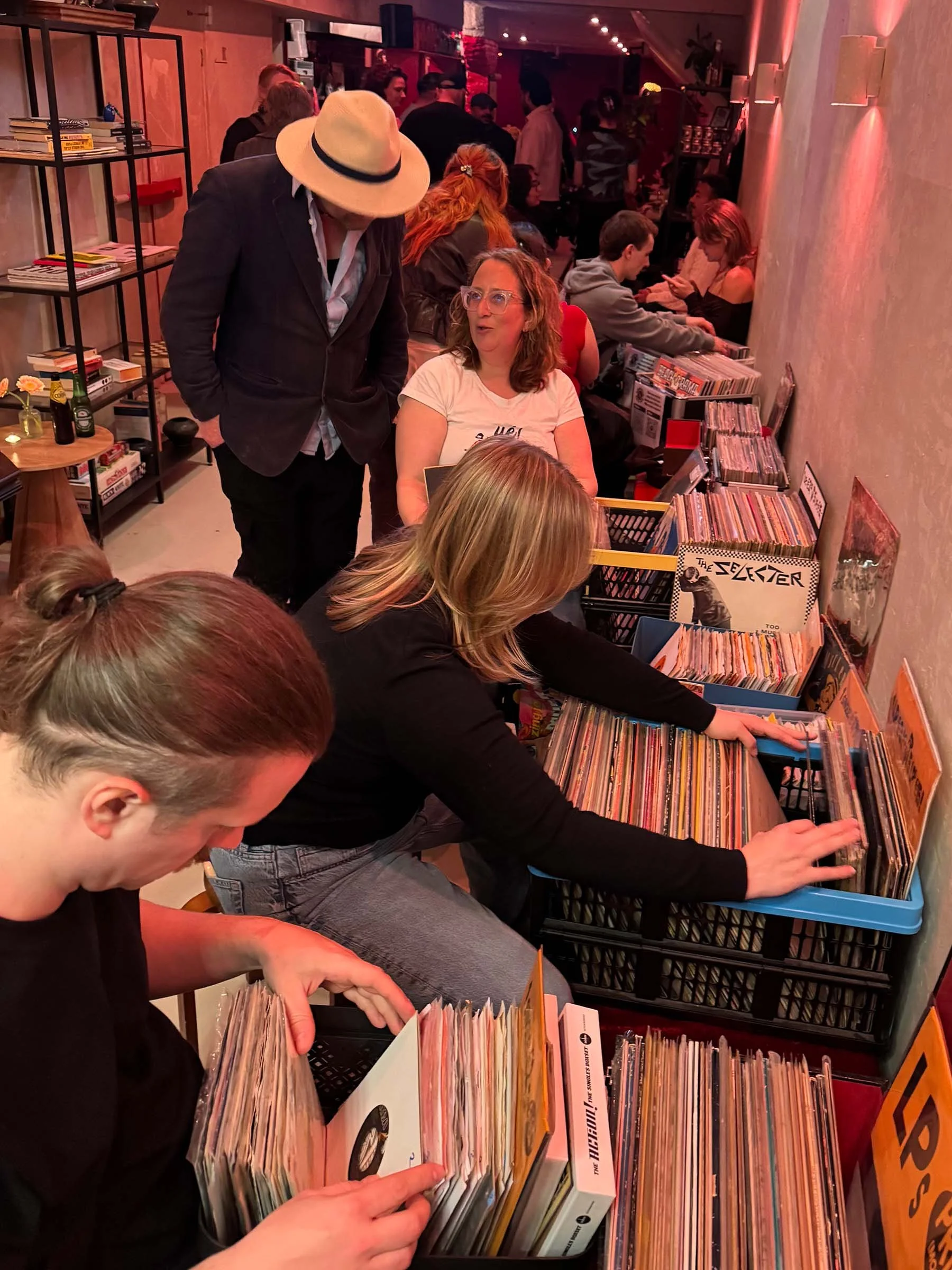 People browsing and selecting records at a vinyl record store or event, with shelves filled with music albums and people engaged in choosing music.