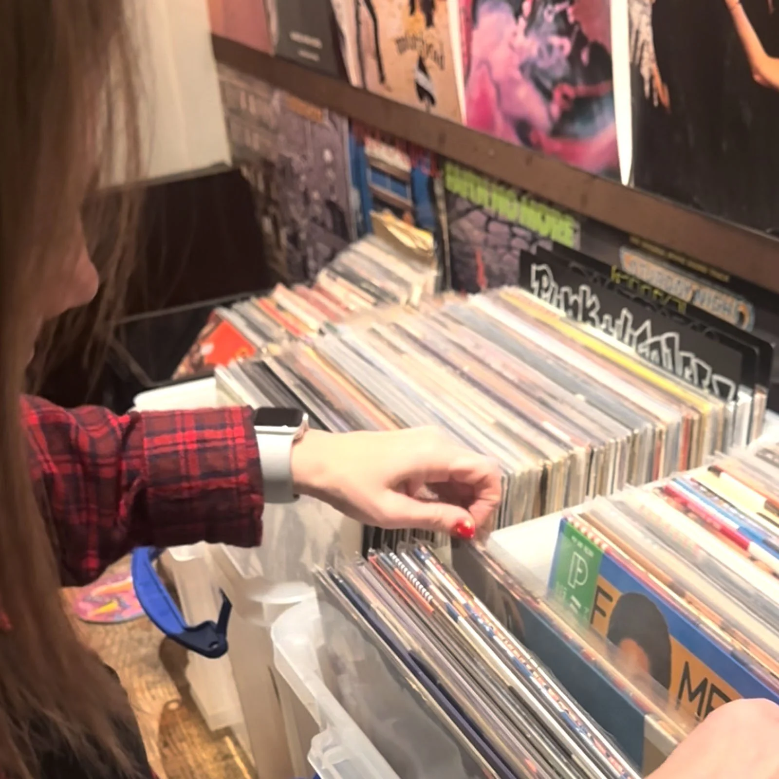 Person browsing through a collection of vinyl records at an Amsterdam Vinyl Club live event, with shelves filled with albums in the background.