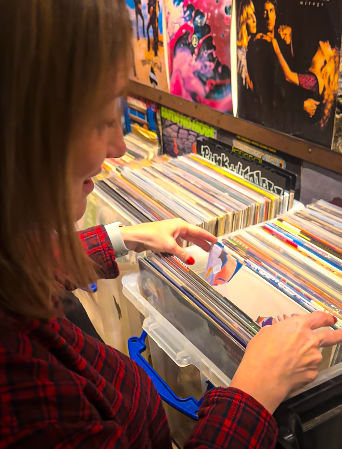 A woman in a red plaid shirt looking through a large collection of vinyl records at Amsterdam Vinyl Club.