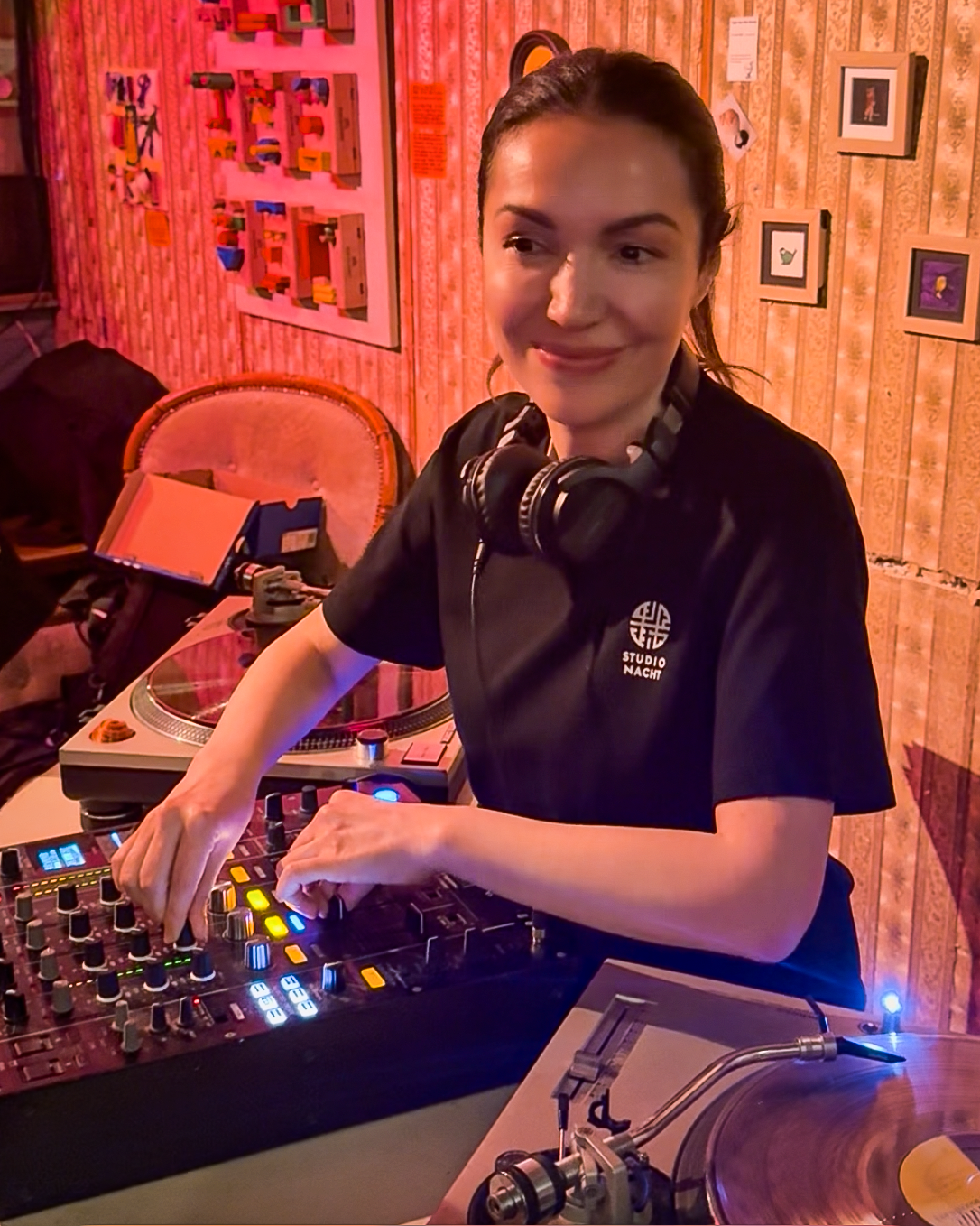 Sophia Sigma playing a guest DJ set at Amsterdam Vinyl Club. She's wearing headphones around her neck and a black T-shirt.