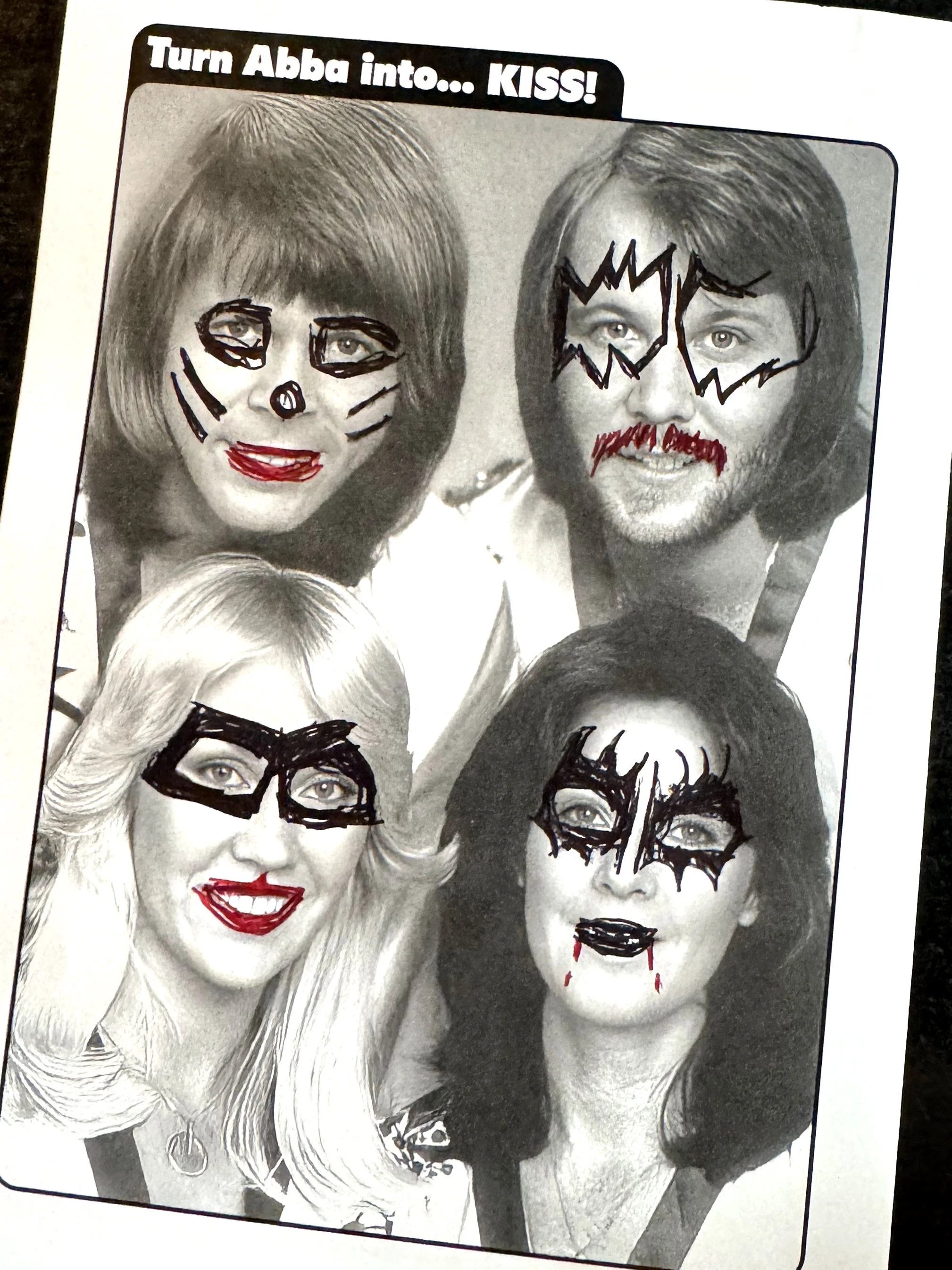 Black and white photo of five women with face paint and drawings added to make them look like comic book characters with lipstick and masks, with the caption "Turn Alba into... KISS!"
