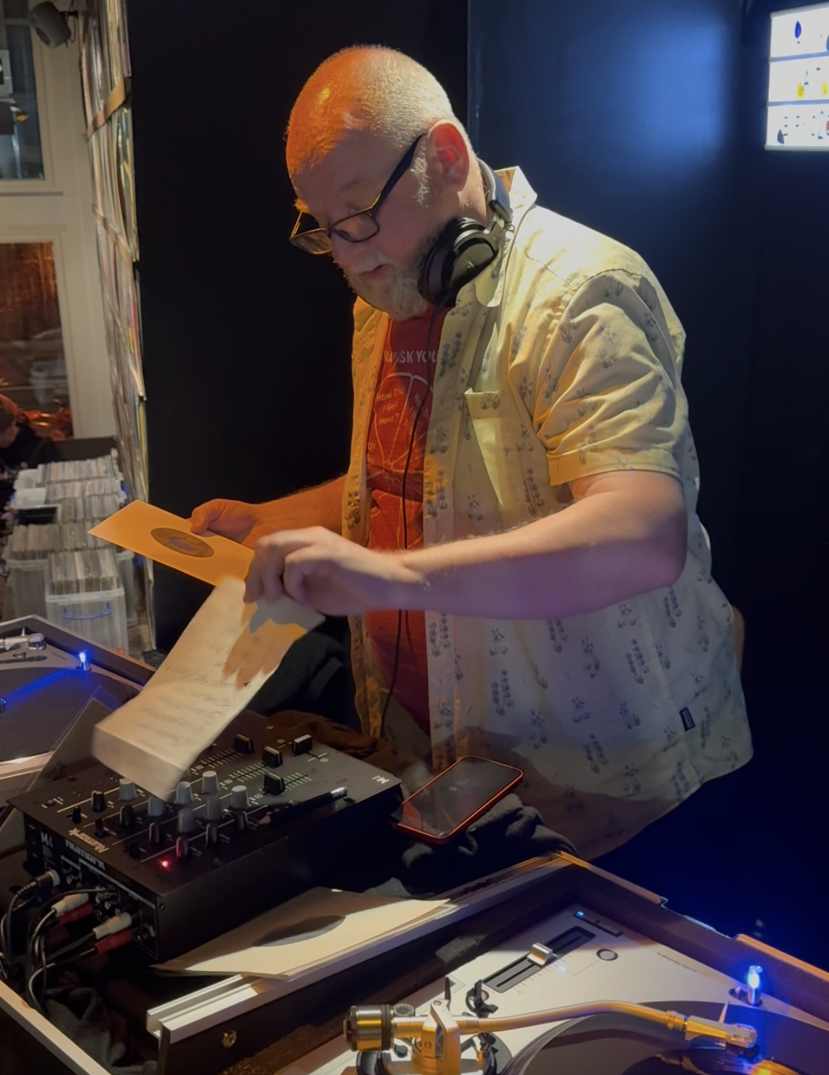 DJ Roland playing a guest DJ set at Amsterdam Vinyl Club. He's wearing headphones around his and a green shirt.