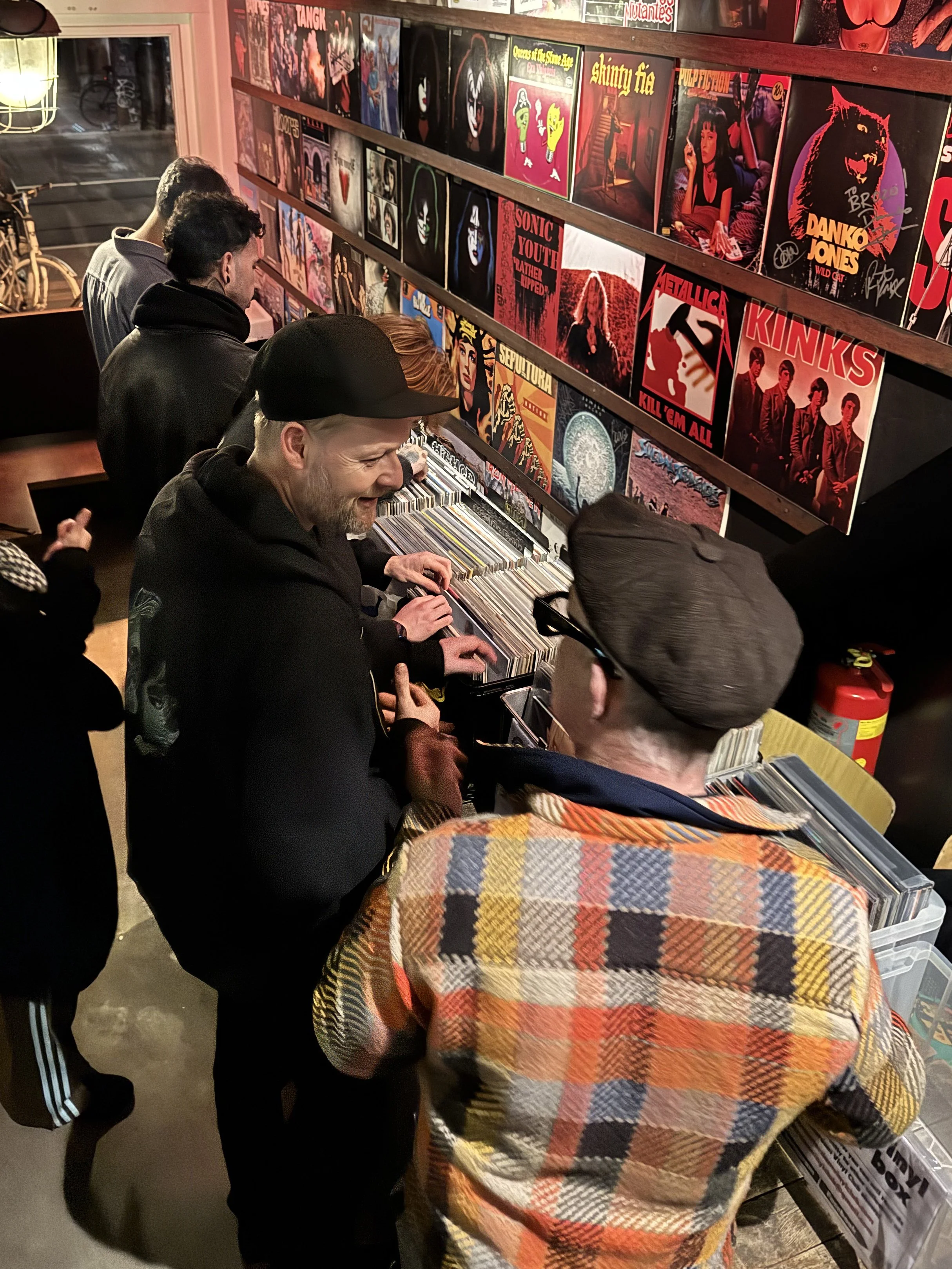 People browsing vinyl records in a store with wall art and album covers displayed.