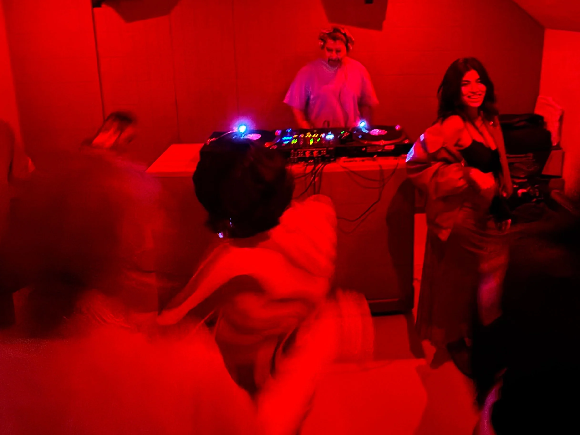 People dancing at an Amsterdam Vinyl Club monthly event in a city venue - people gathered in a dimly lit room with red lighting, sitting around tables, some eating and socializing.