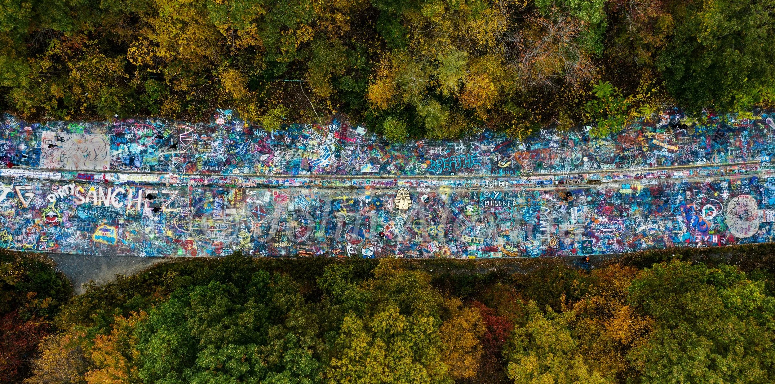 04 · A Trace Through the Landscape: A panoramic aerial view of the painted roadway and surrounding woodland in Centralia, Pennsylvania, 2019.

© John Alexiou · 2019 · Centralia