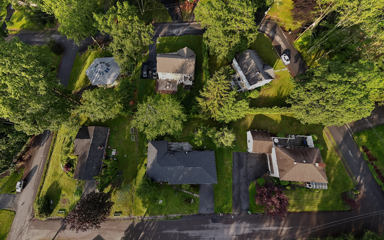 An aerial view of a residential neighborhood showing six houses, lush green trees, driveways, parked cars, and well-maintained lawns.
