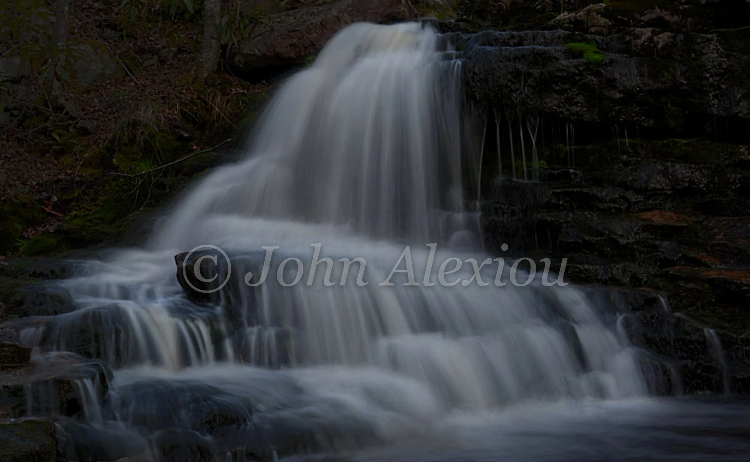 05 · Over the Dark Shelves
A broad fall pours across layered rock, with thin streams tracing the shaded ledges.
© John Alexiou · 2026 · Northeast Pennsylvania