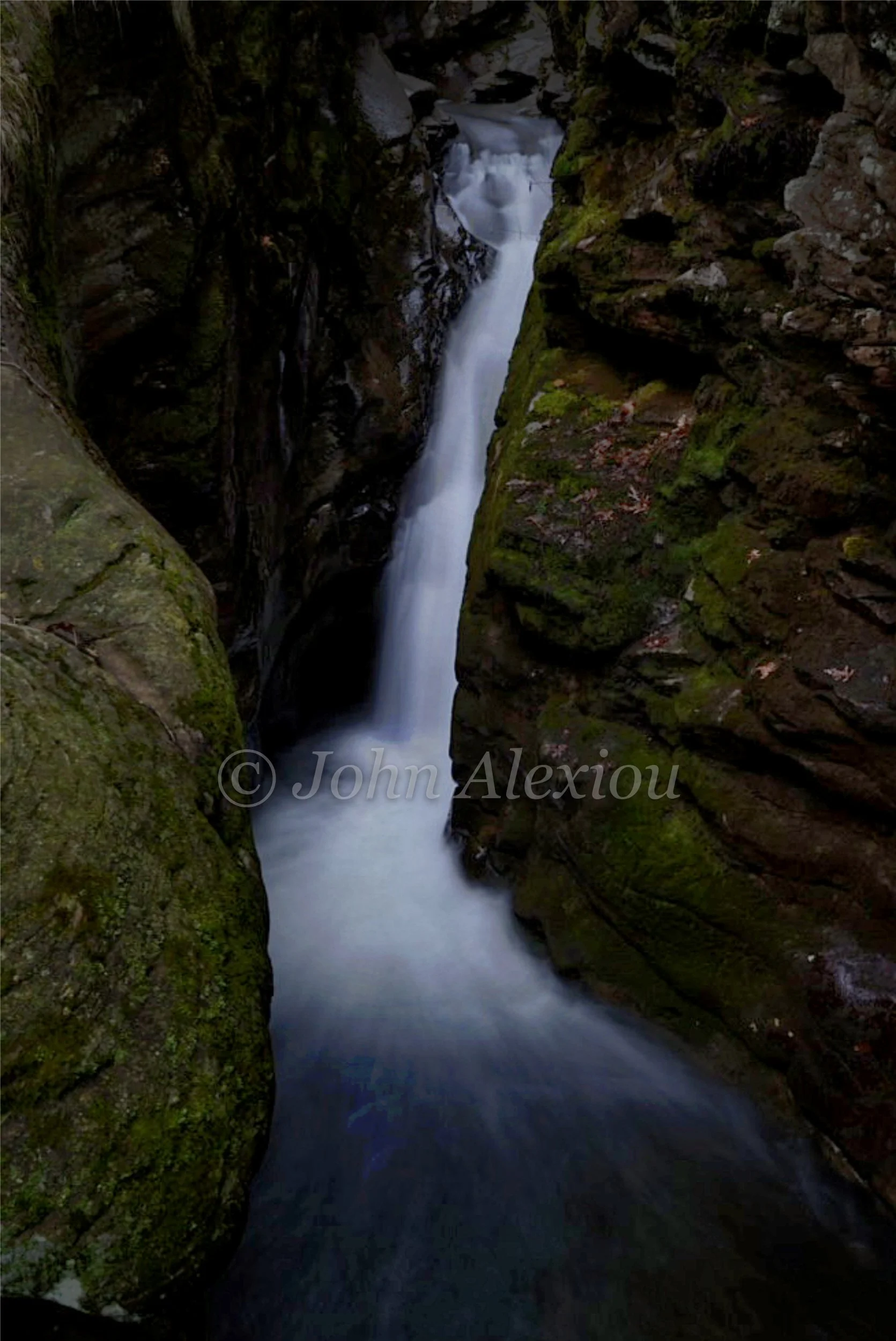 02 · Through the Narrow Walls
A slender waterfall drops between moss-covered rock walls and opens into a dark pool.
© John Alexiou · 2026 · Northeast Pennsylvania