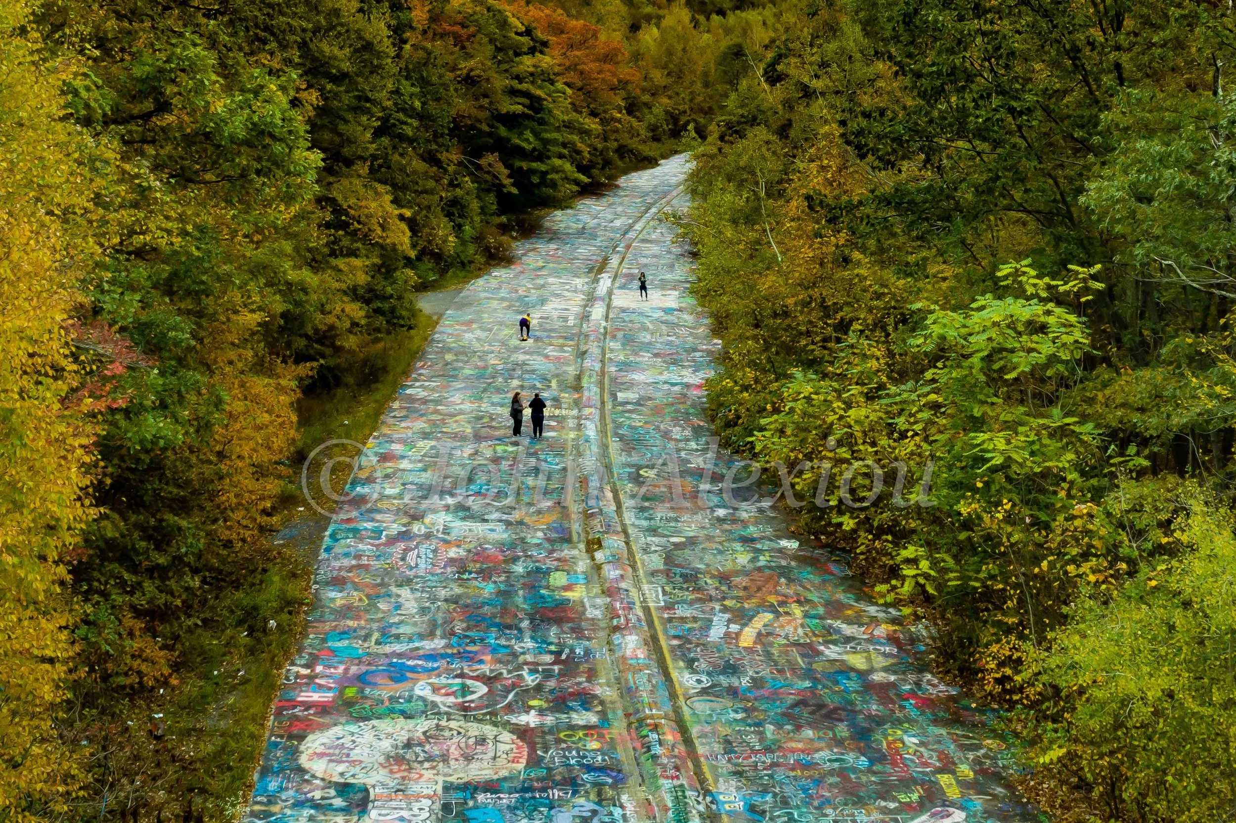02 · Walking the Canvas: Visitors follow the colorful abandoned roadway into the forest at Graffiti Highway, Centralia, Pennsylvania, 2019.

© John Alexiou · 2019 · Centralia