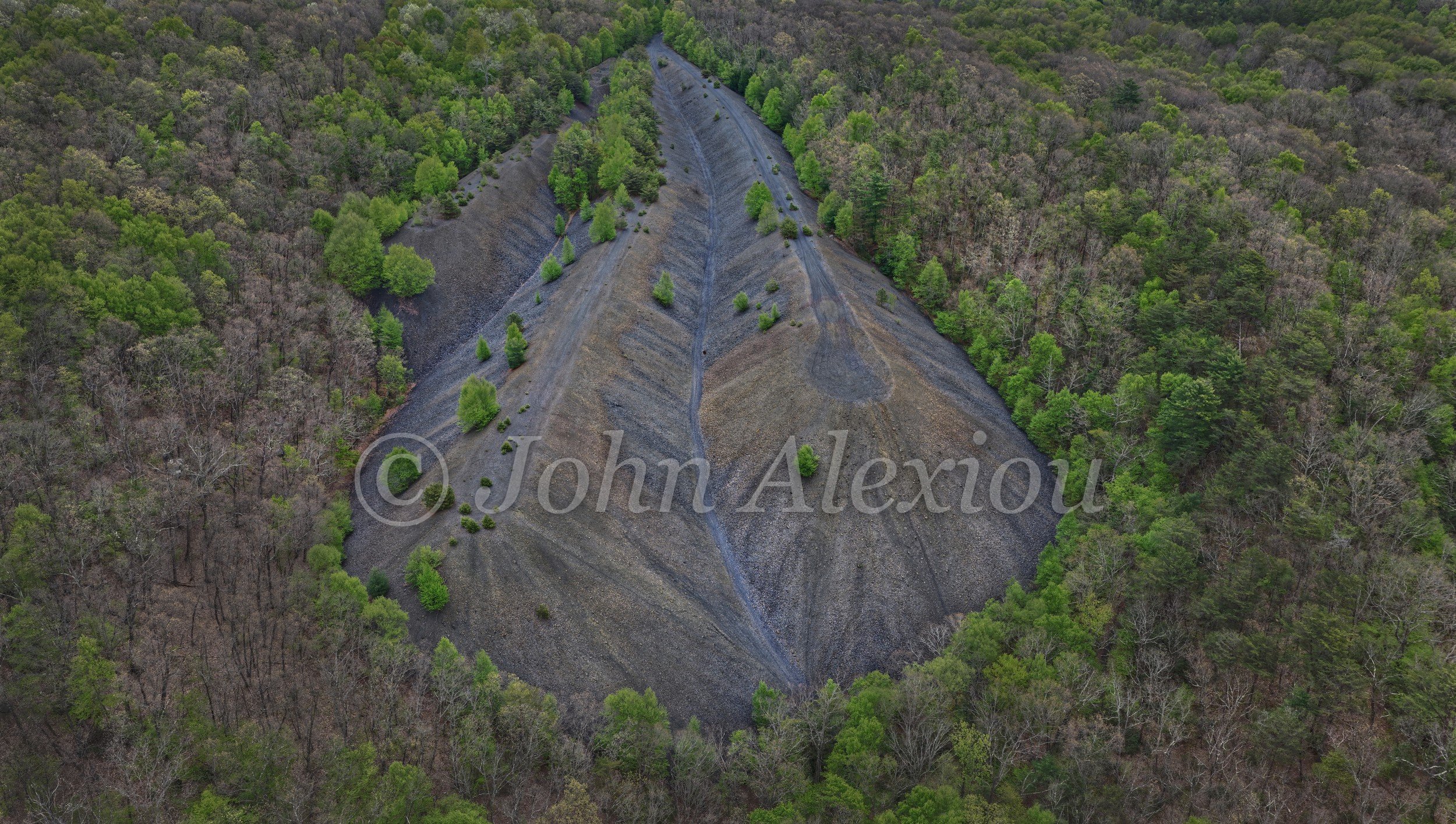 10 · The Forest Moves In: An aerial view of a dark triangular bank surrounded by returning green woodland.

© John Alexiou · 2025 · Mocanaqua