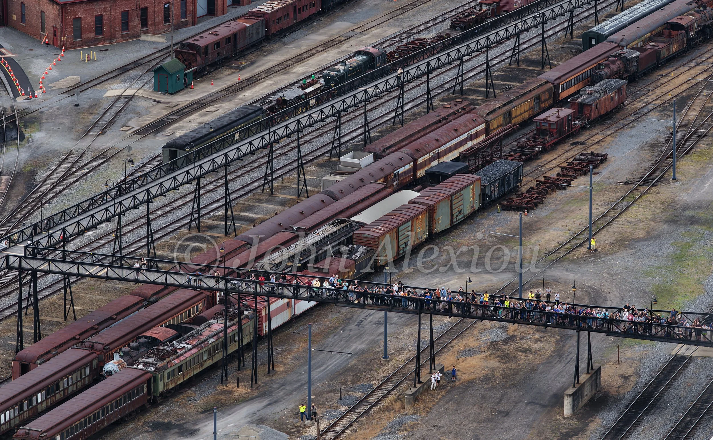 07 · Everyone Finds a View
A wider view of the rail yard brings together the crowded walkway, stored rolling stock, and Big Boy in the distance.
© John Alexiou · 2026 · Steamtown, Scranton