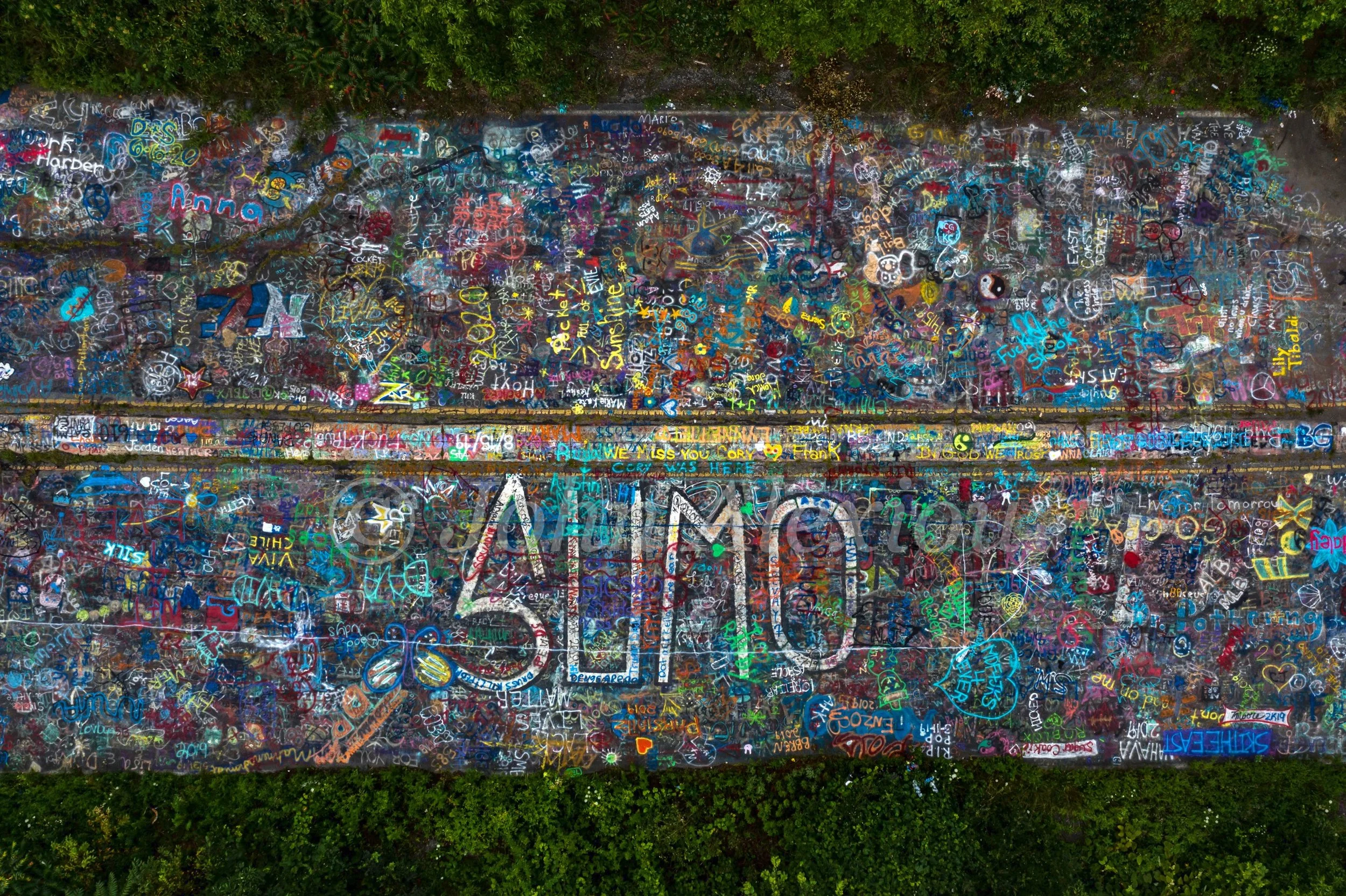 07 · Painted Voices: An overhead field of layered lettering and colorful graffiti along the center lines of Graffiti Highway, Centralia, Pennsylvania, 2019. Reviewed presentation version.

© John Alexiou · 2019 · Centralia