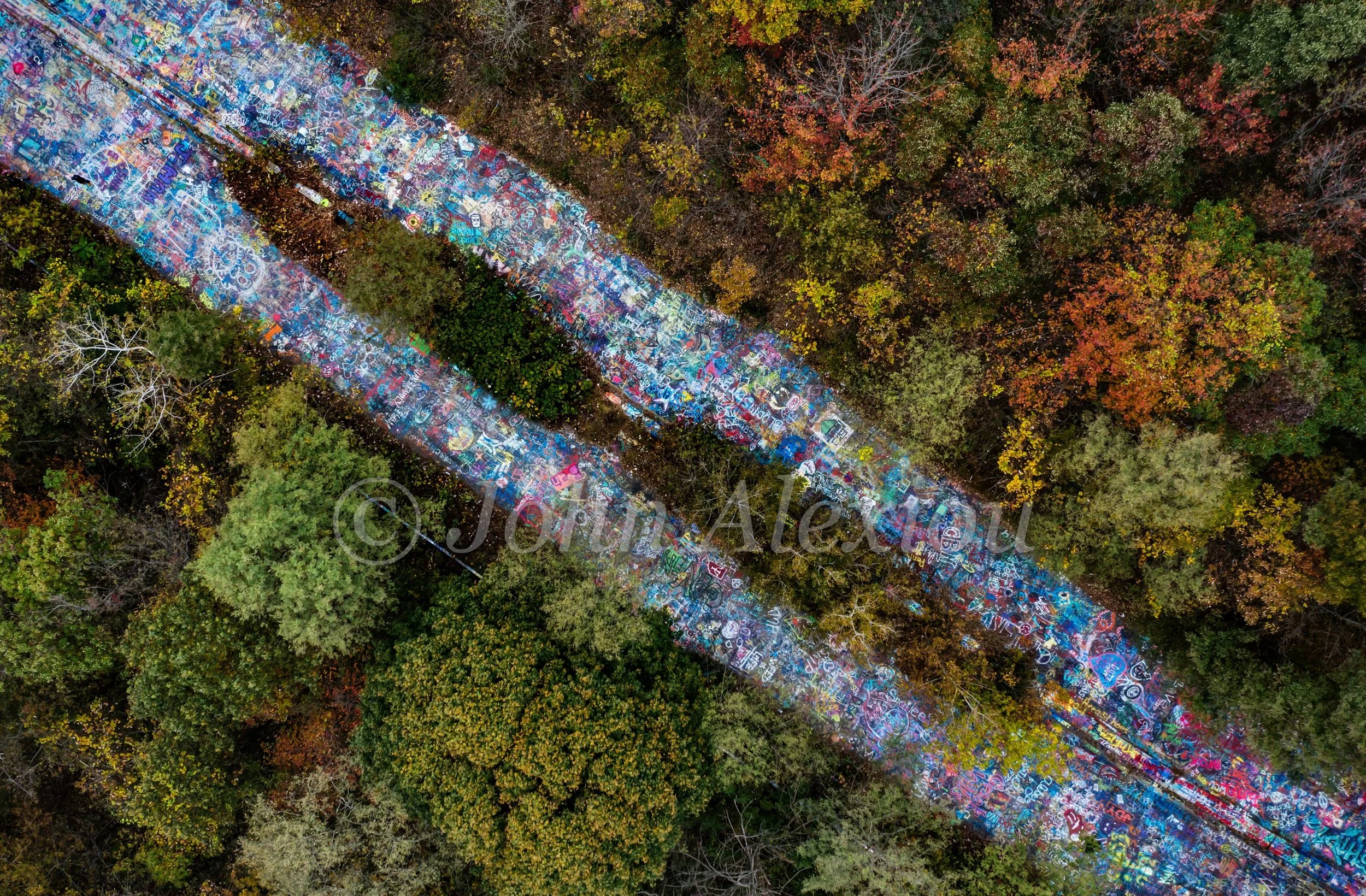 03 · Between the Trees: Diagonal aerial view of twin painted lanes through autumn woodland at Graffiti Highway, Centralia, Pennsylvania, 2019.

© John Alexiou · 2019 · Centralia