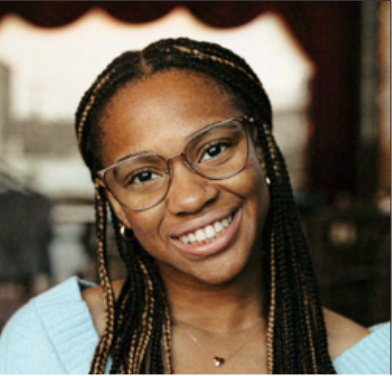 Young woman with glasses and braided hair smiling indoors.