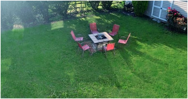 A round outdoor table with a grill and six pink chairs on a grassy lawn near a house.