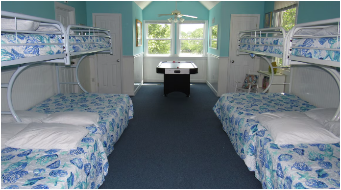 Bunk beds with seashell and ocean-themed bedding in a brightly lit room with blue walls and windows.