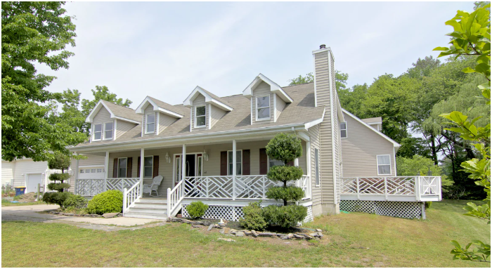 Large two-story house with a front porch, multiple dormer windows, and a decorated lawn in a suburban neighborhood.